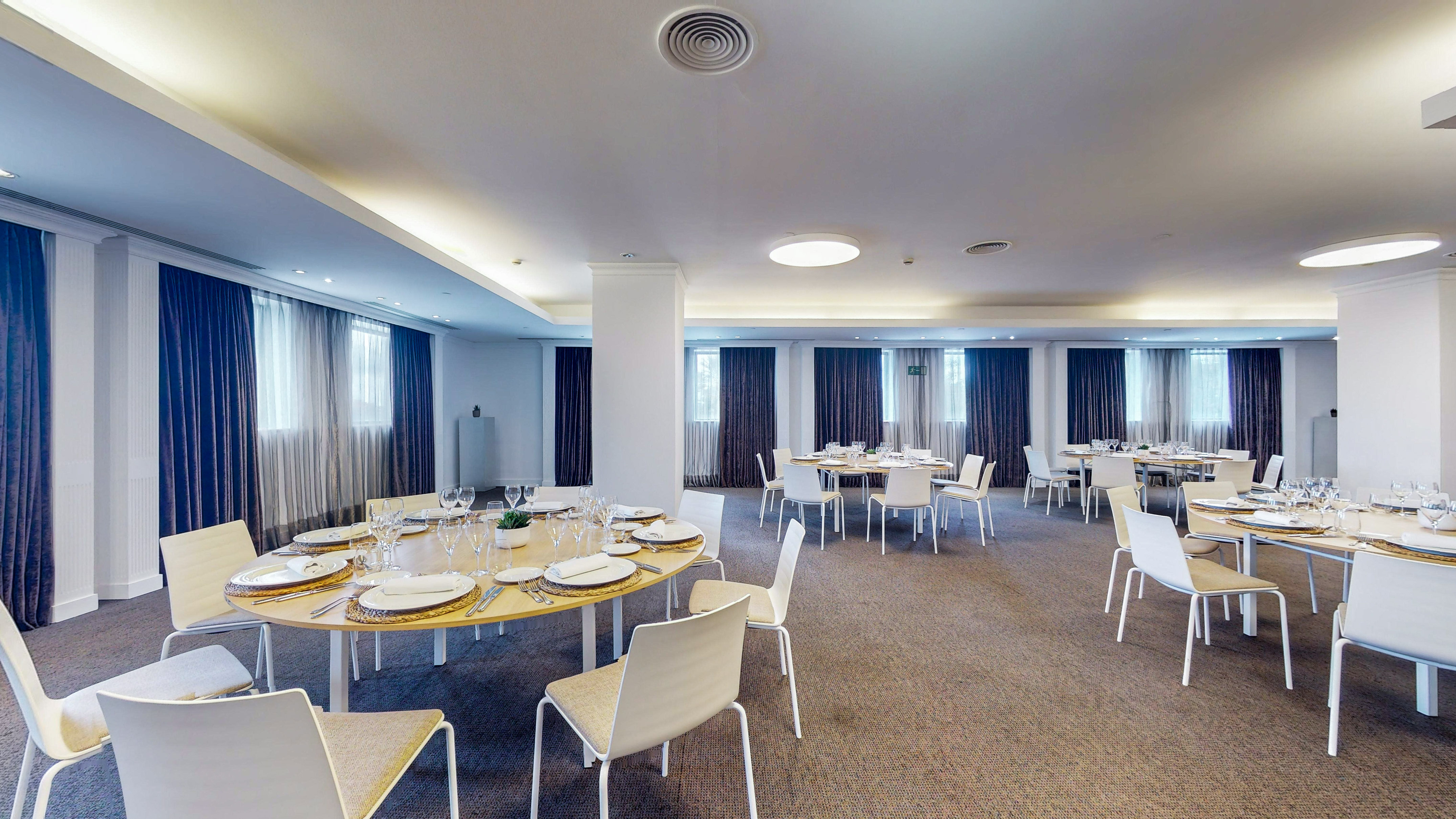 Spacious event room with round dining tables, modern chairs, and dark curtains.