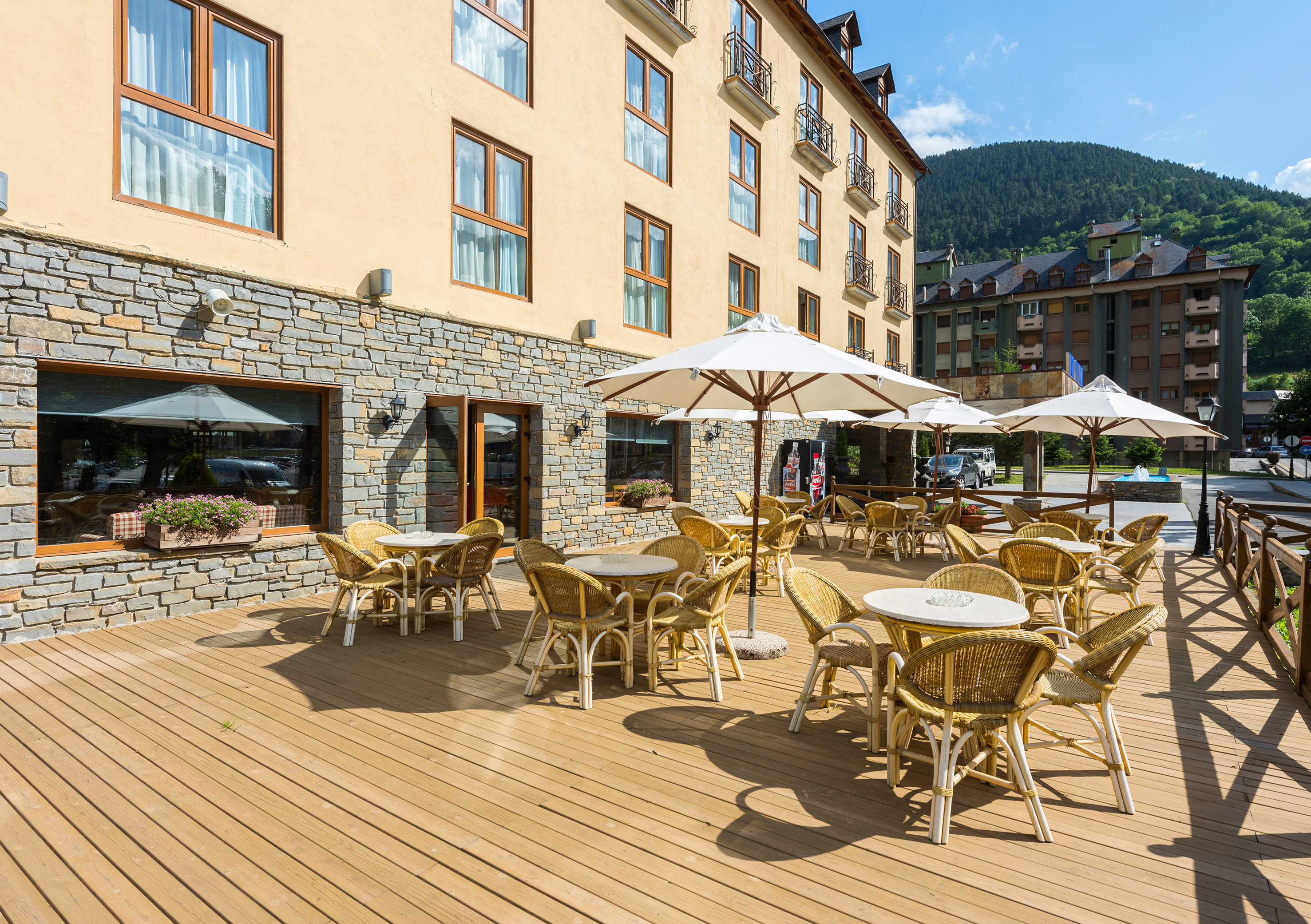 Hotel outdoor terrace with wicker tables, chairs, white umbrellas, and mountain view.