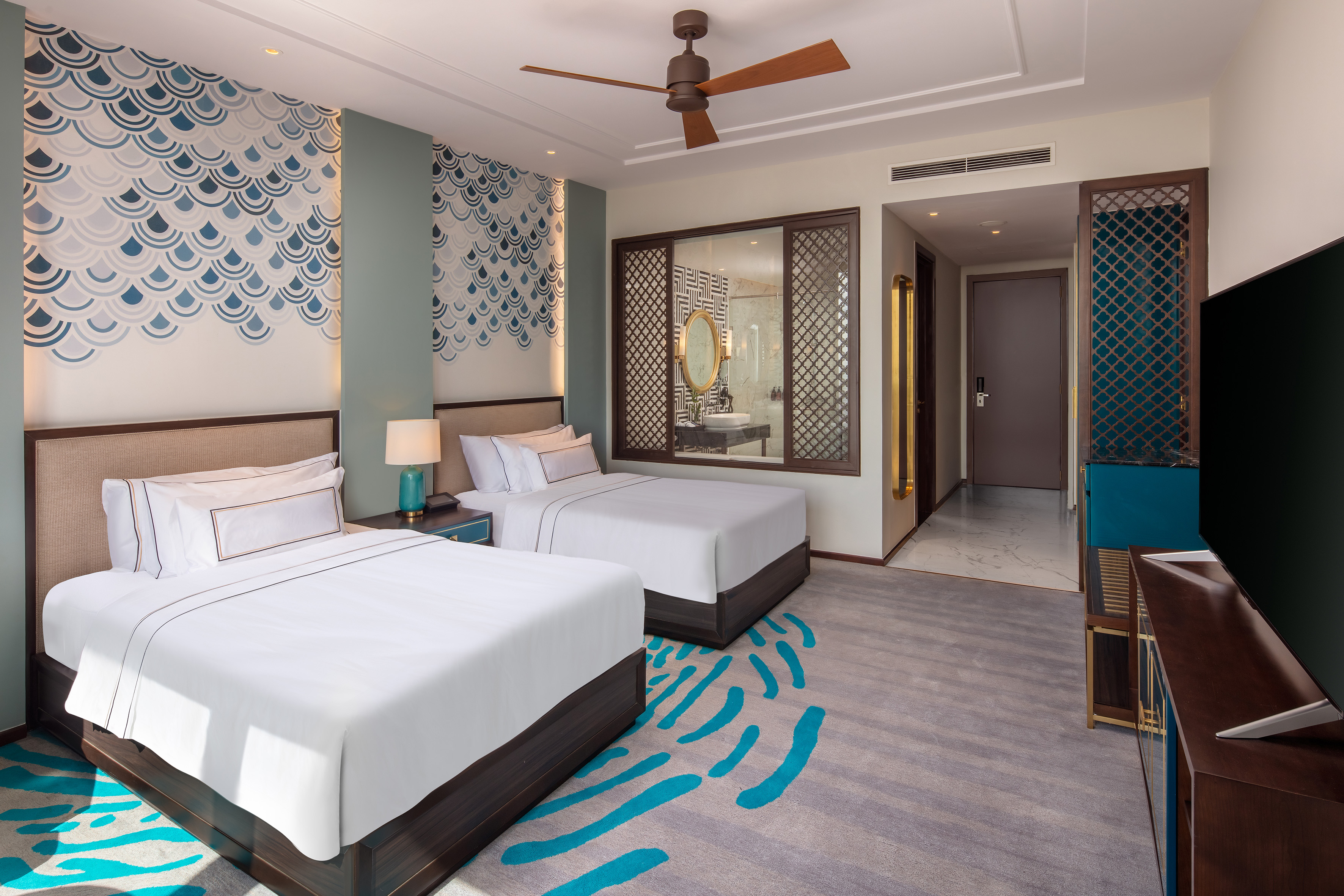Modern hotel room with two beds, blue wave accent wall, and wood ceiling fan.