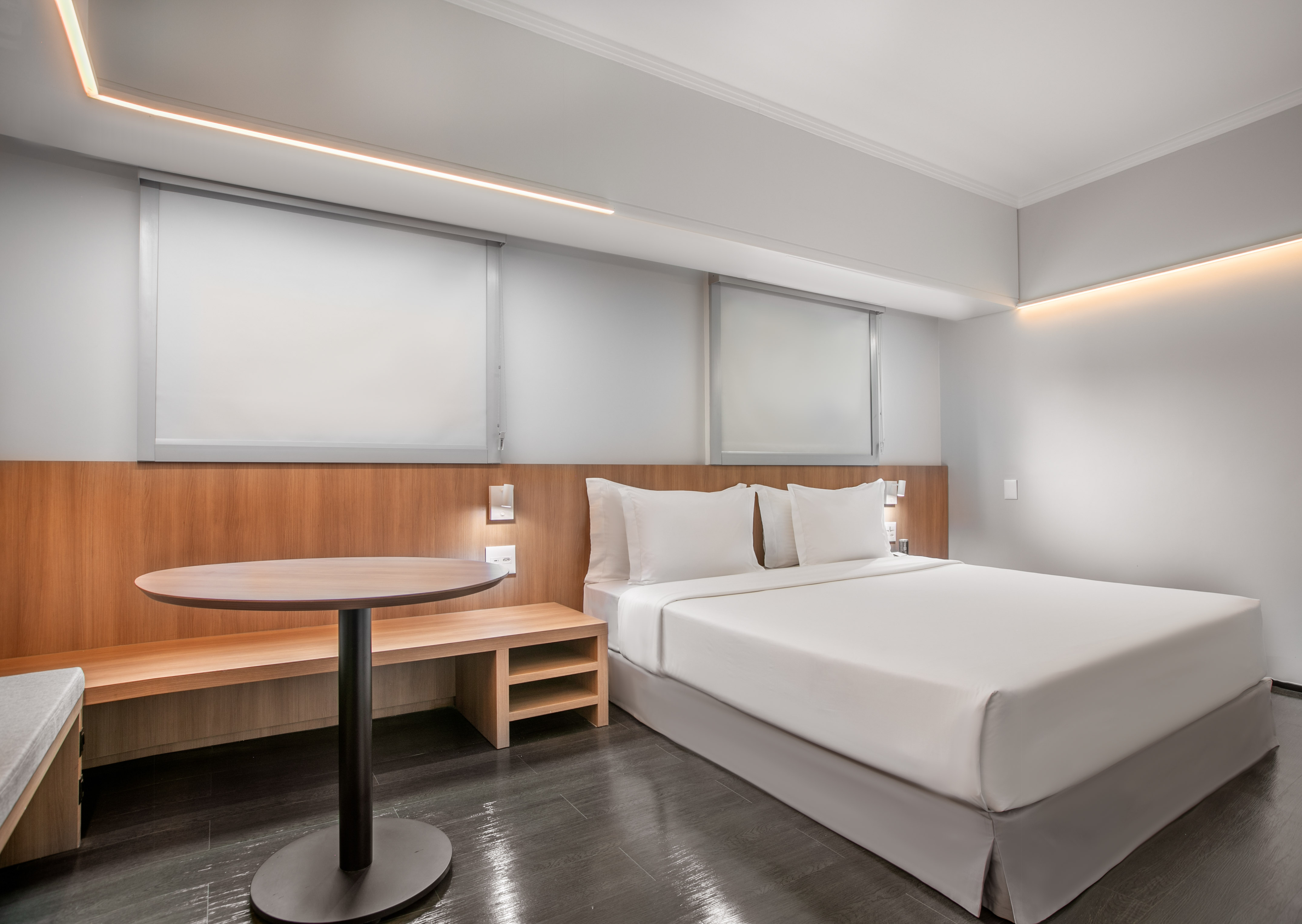 Modern hotel room with white bed, wooden accents, round table, and recessed lighting.