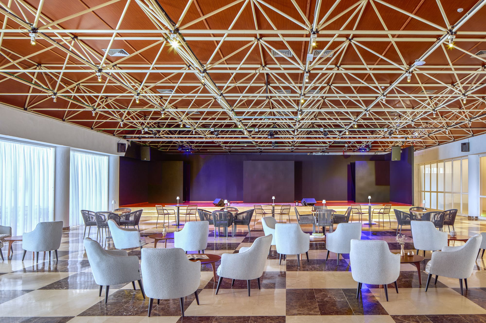 Modern event lounge with stage, comfortable seating, and exposed truss ceiling.