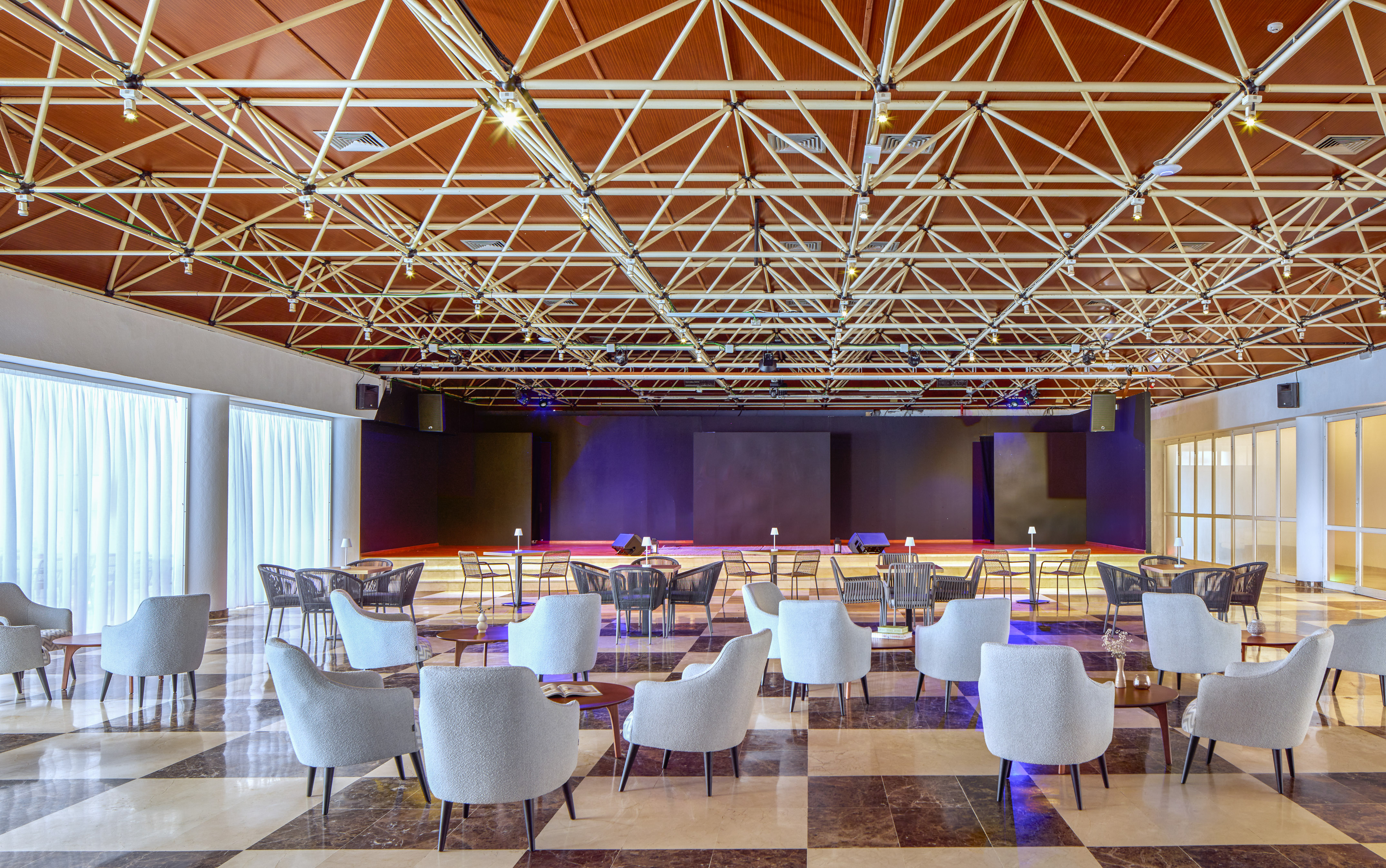 Modern event lounge with stage, comfortable seating, and exposed truss ceiling.