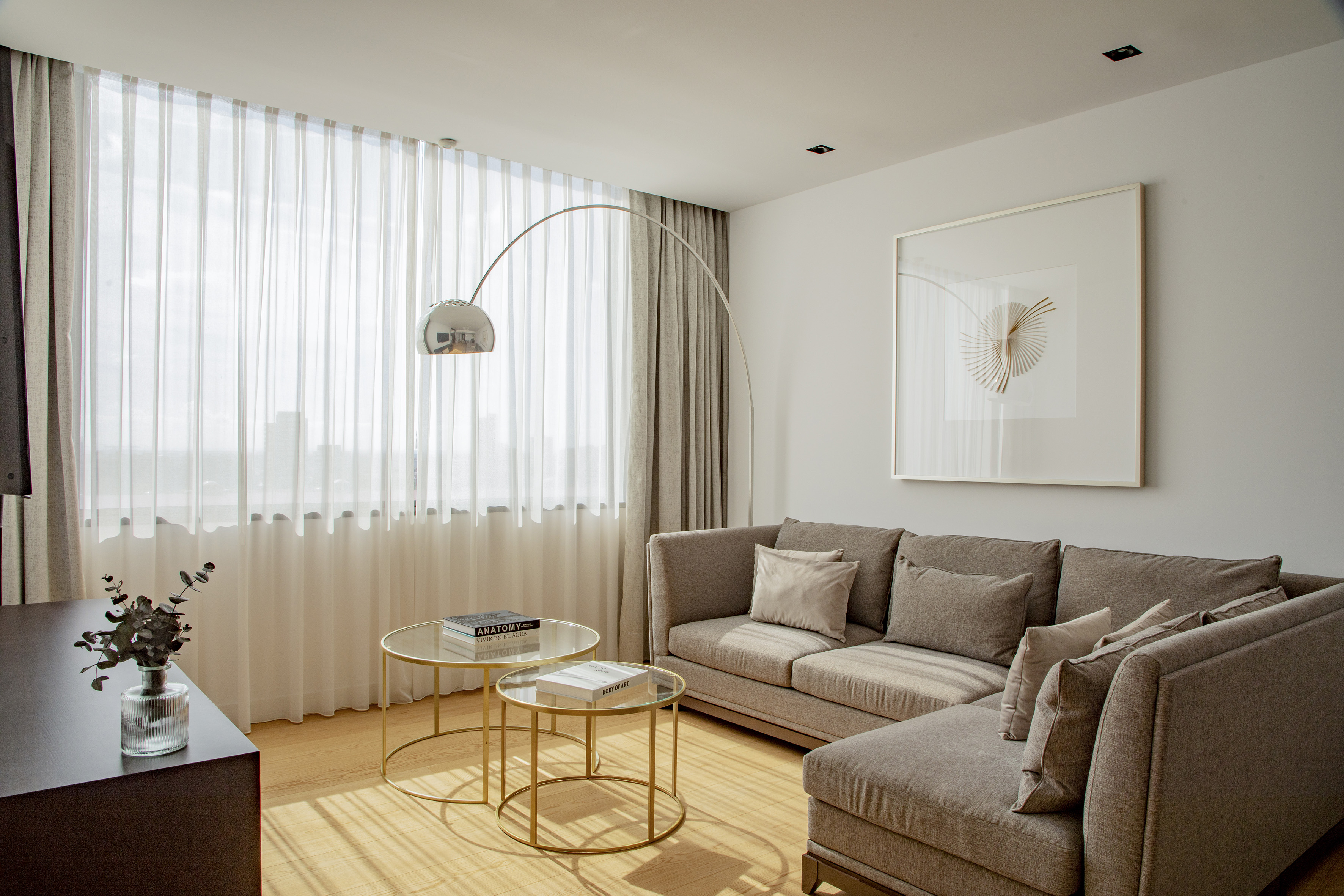 Stylish living room with L-shaped sofa, glass tables, arc lamp, large window.