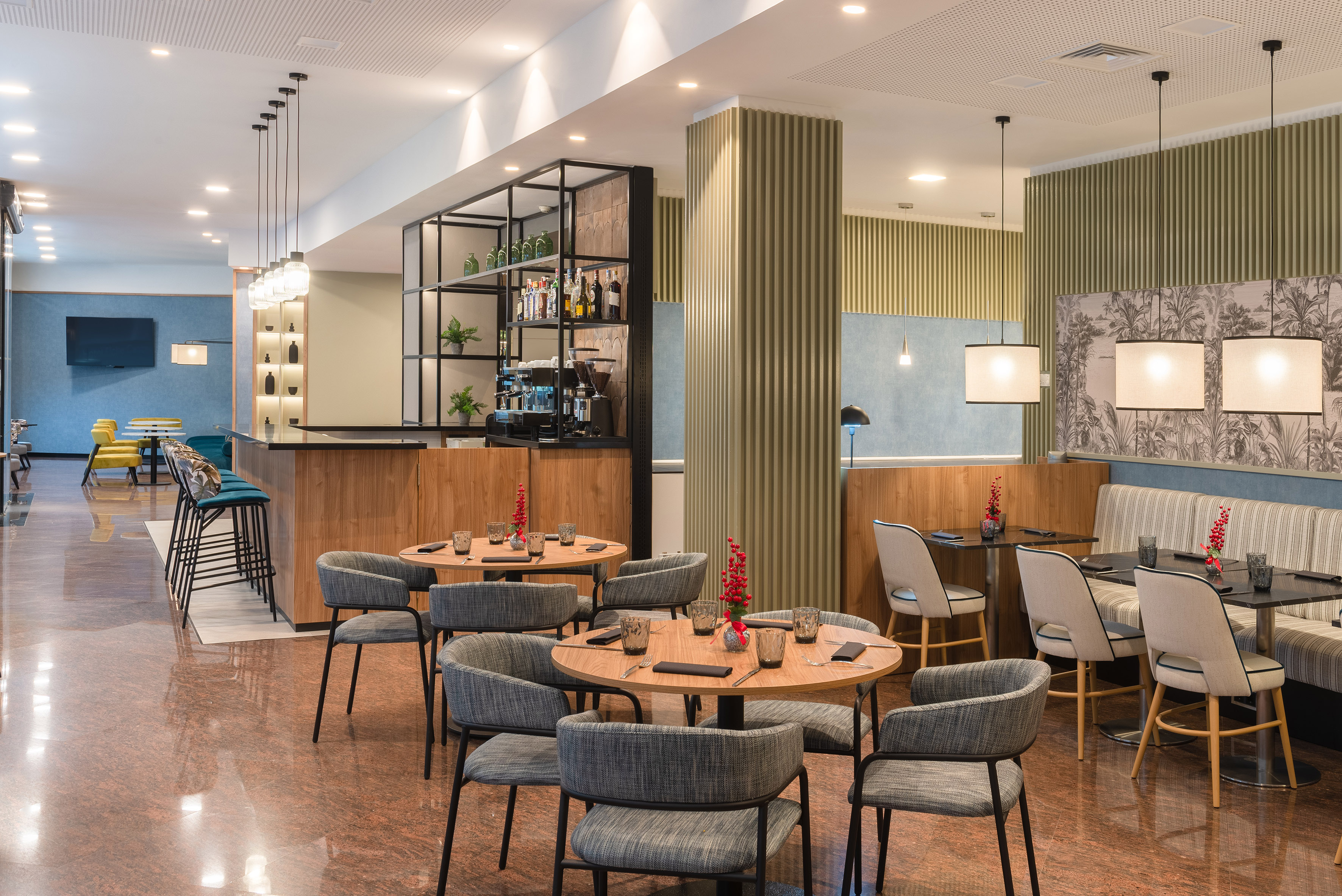 Modern hotel restaurant with bar, round tables, grey chairs, and patterned walls.