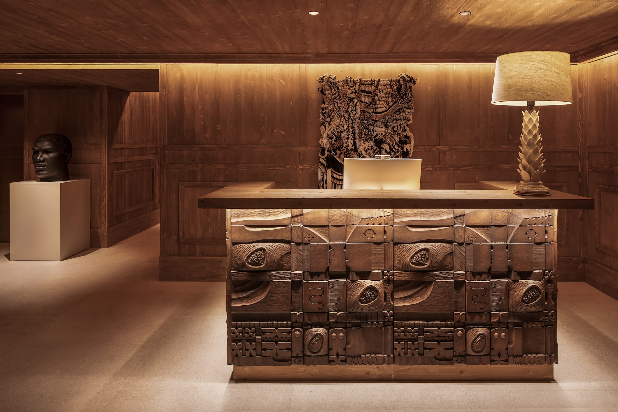 Wooden reception desk with carved details and warm lighting in a hotel lobby.