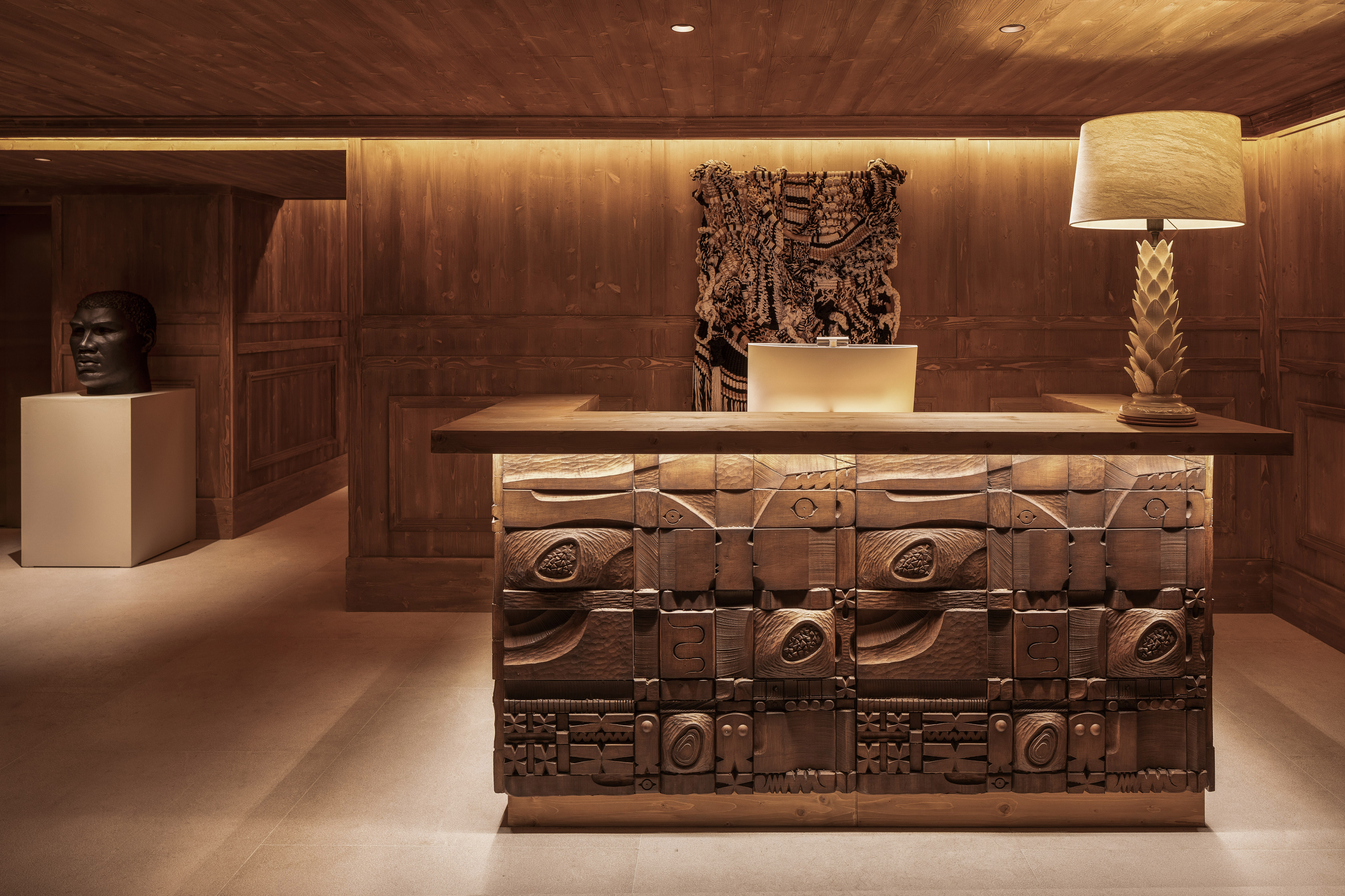 Wooden reception desk with carved details and warm lighting in a hotel lobby.