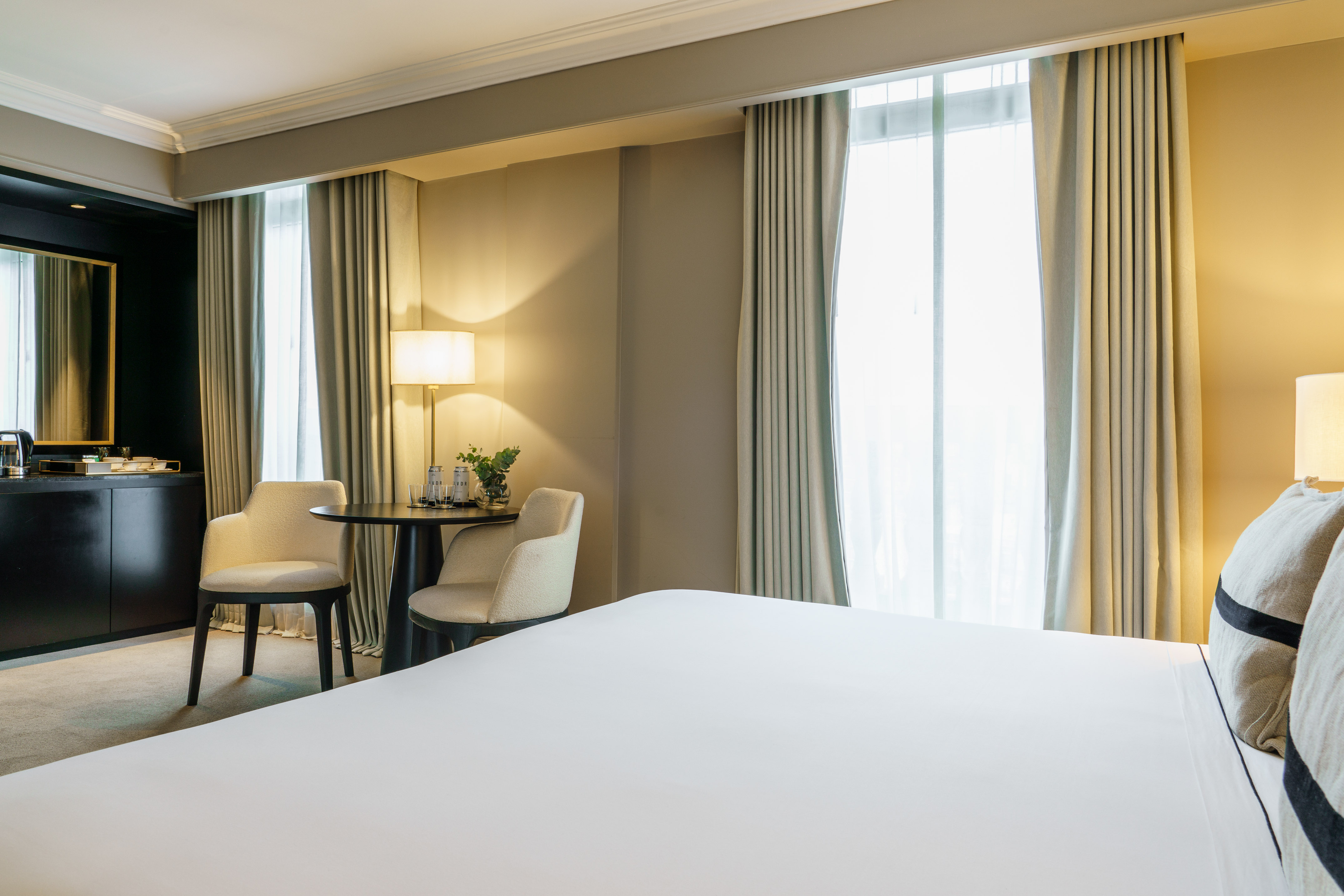 Luxury hotel room with white bed, table, two chairs, and large window.