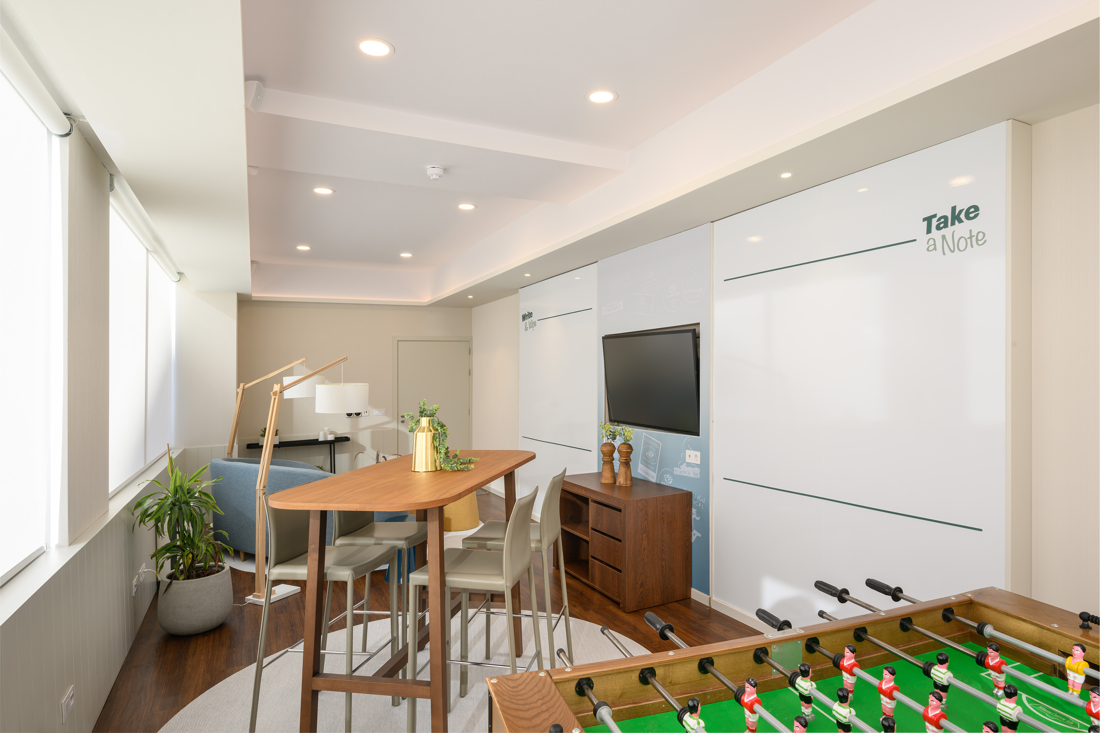 Bright modern office lounge with foosball, high bar table, and whiteboard walls.