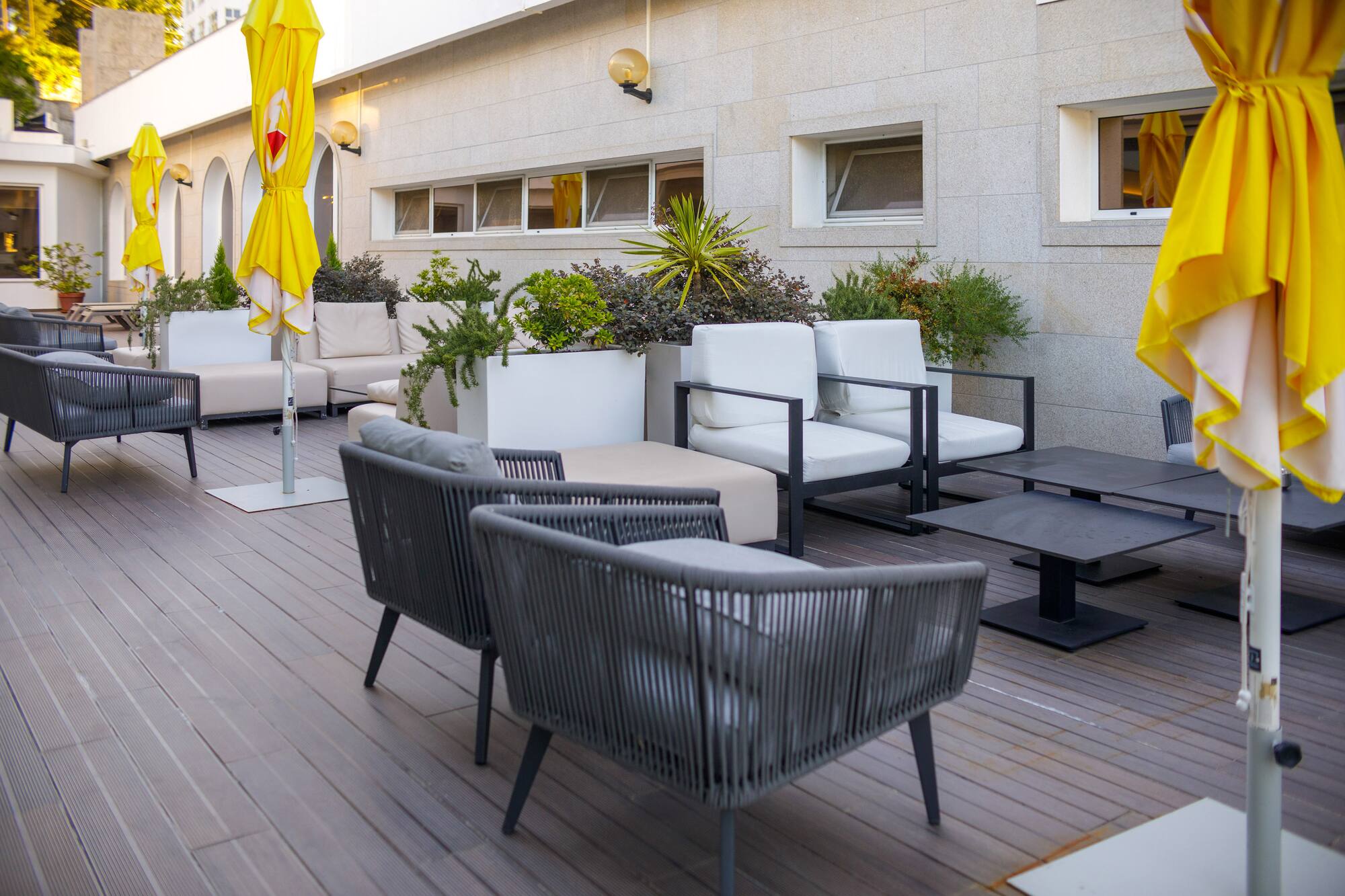 Modern outdoor patio with grey and white lounge furniture, yellow umbrellas, plants.