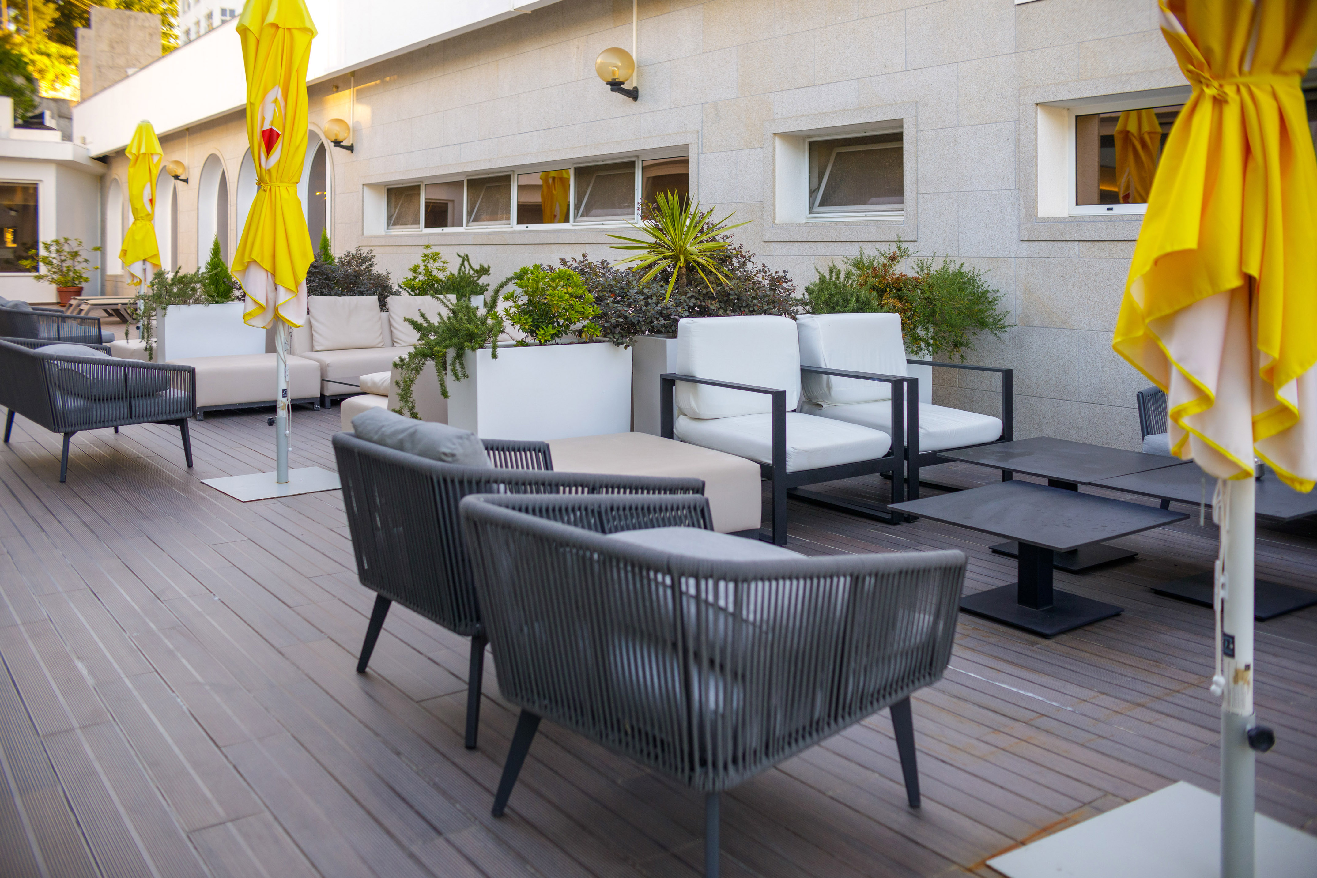 Modern outdoor patio with grey and white lounge furniture, yellow umbrellas, plants.