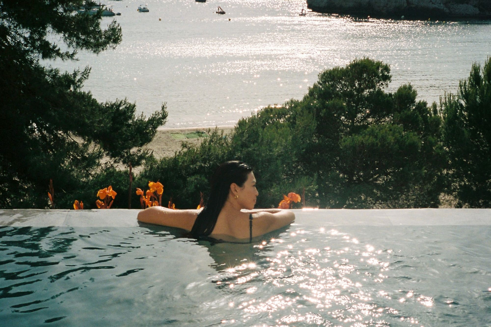 Mujer relajándose en piscina infinita con vista a bahía soleada y montañas.