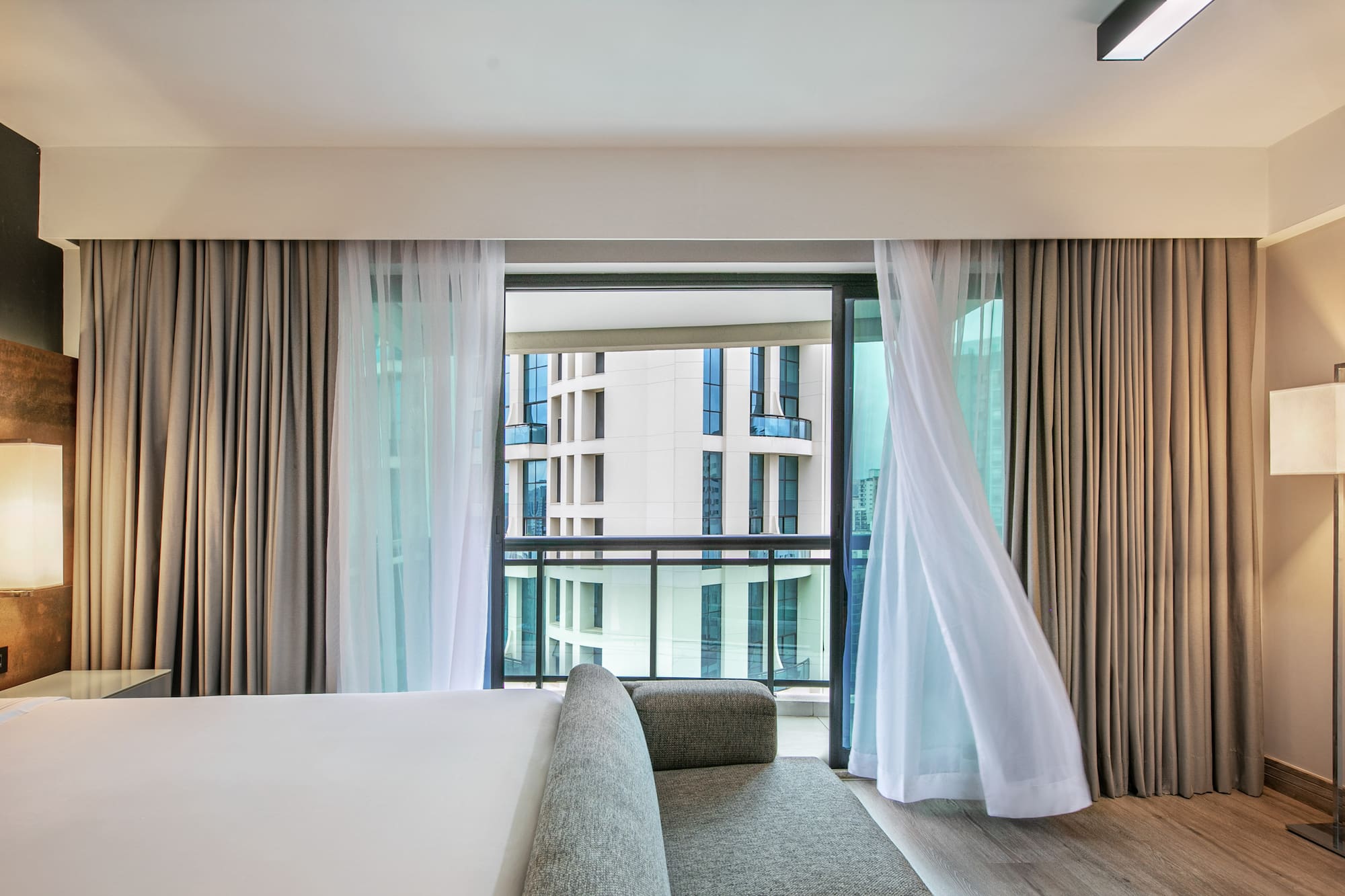 Quarto de hotel moderno com cortinas ao vento e vista para prédios. - Deluxe Queen Room com Varanda - Meliá Ibirapuera, São Paulo