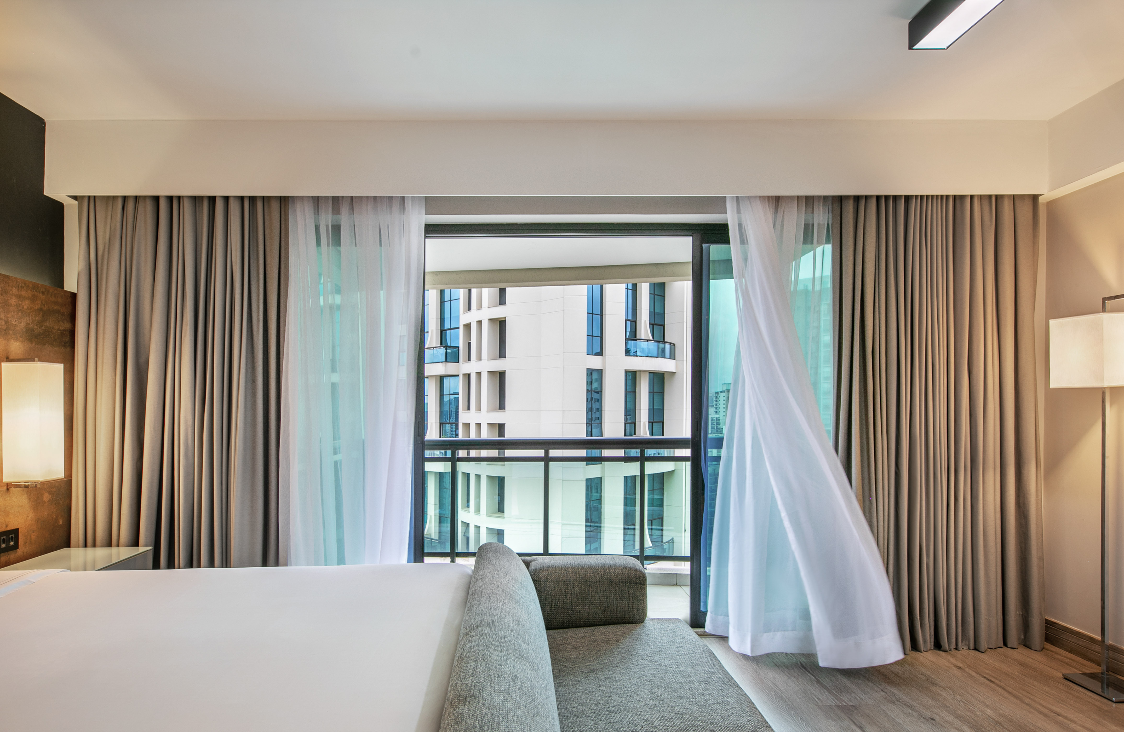 Quarto de hotel moderno com cortinas ao vento e vista para prédios. - Deluxe Queen Room com Varanda - Meliá Ibirapuera, São Paulo