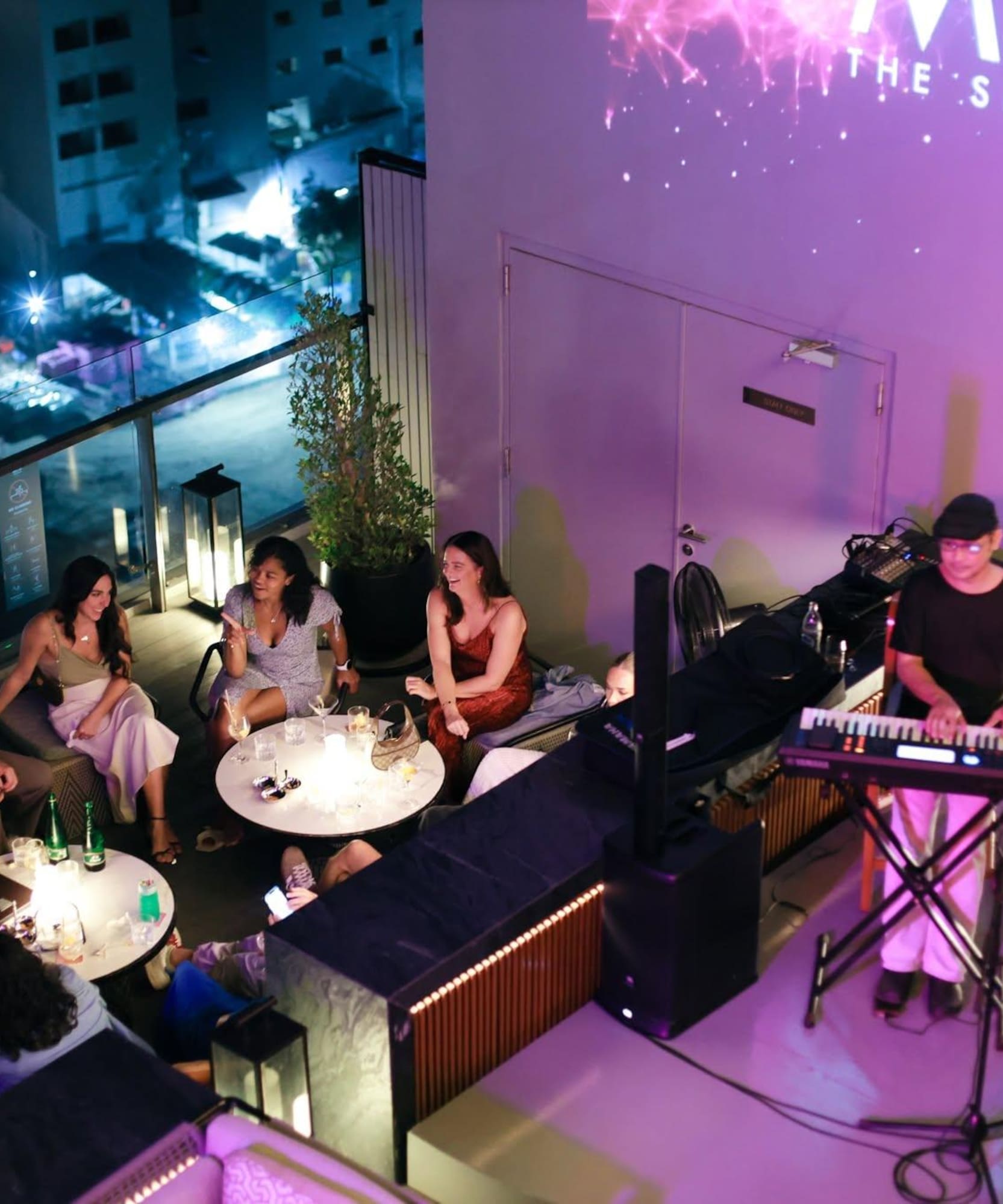 Guests enjoying live music and drinks at a vibrant rooftop sky bar at night.