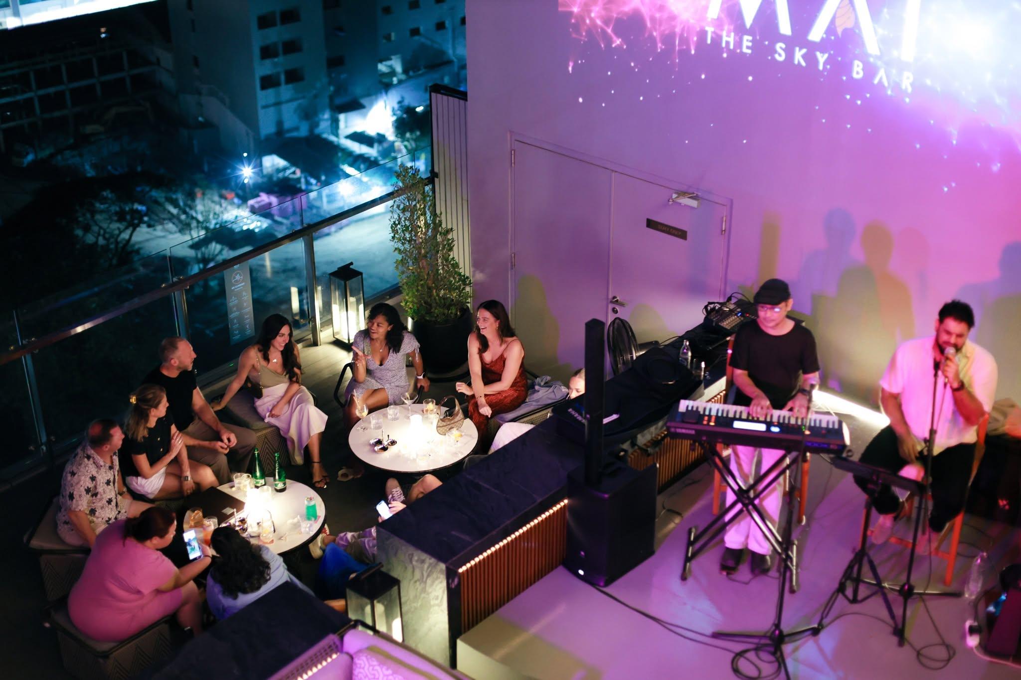 Guests enjoying live music and drinks at a vibrant rooftop sky bar at night.