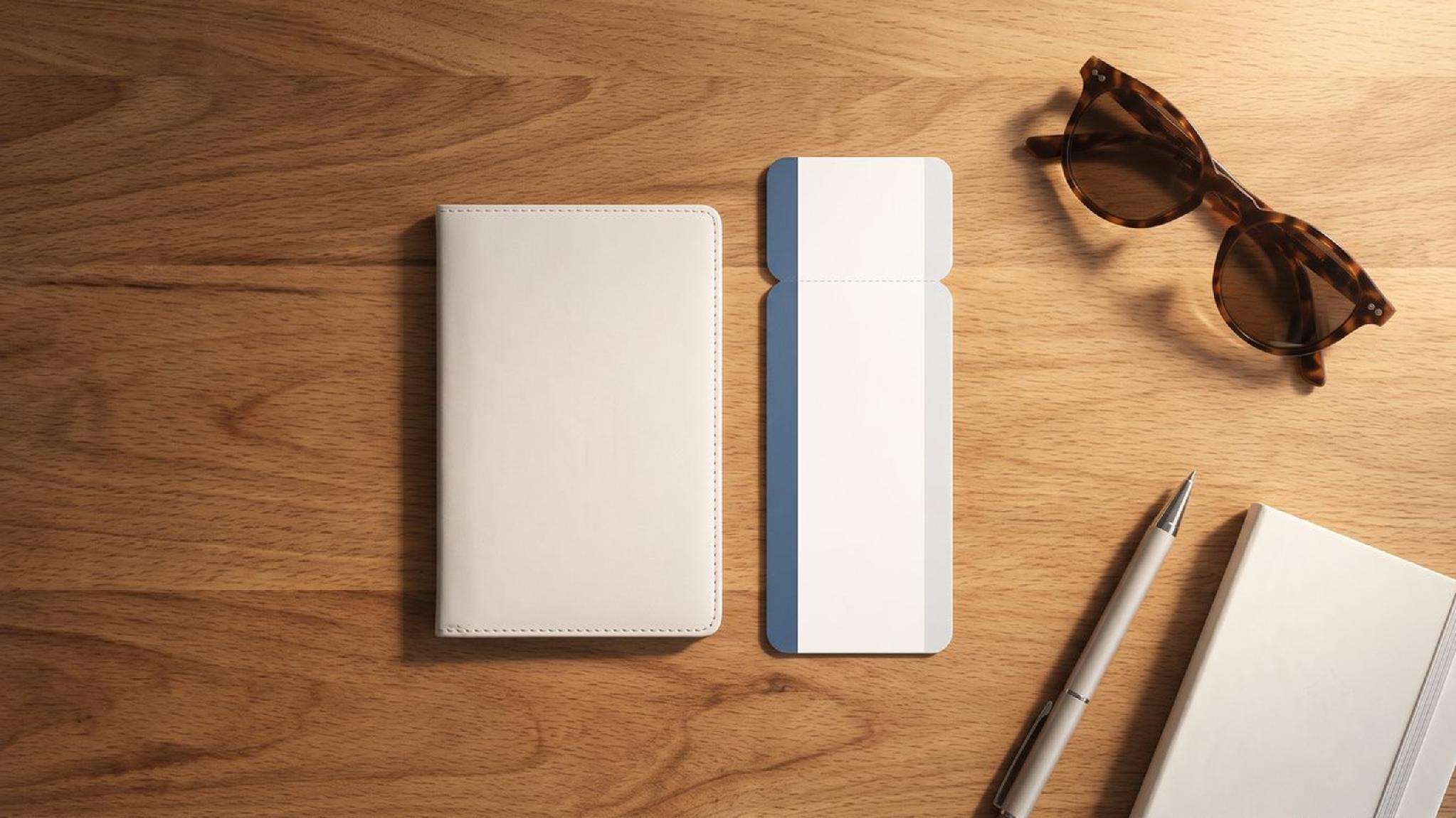 Passport holder, boarding pass, sunglasses, pen, and notebook on wooden desk.