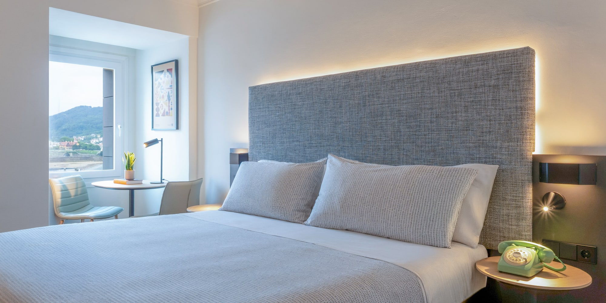 Habitación de hotel moderna con cama doble, cabecero iluminado y vista al mar.