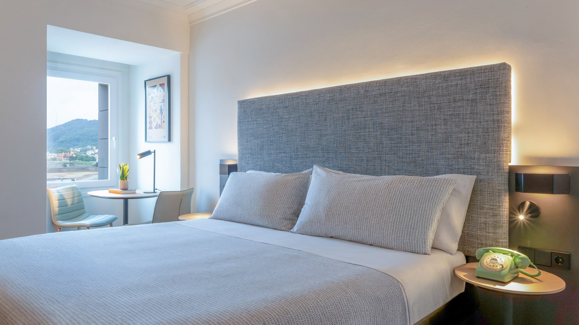 Habitación de hotel moderna con cama doble, cabecero iluminado y vista al mar.