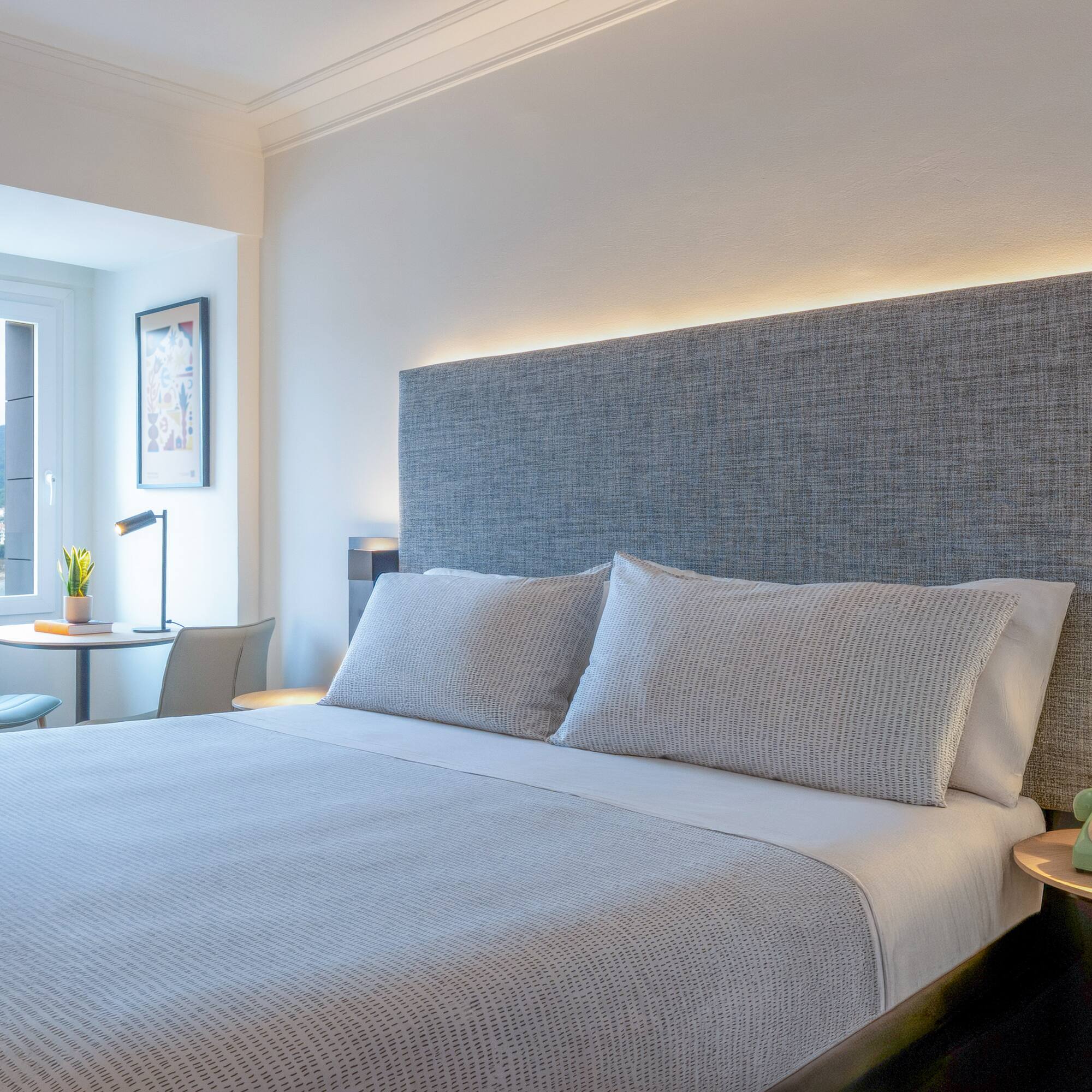 Habitación de hotel moderna con cama doble, cabecero iluminado y vista al mar.