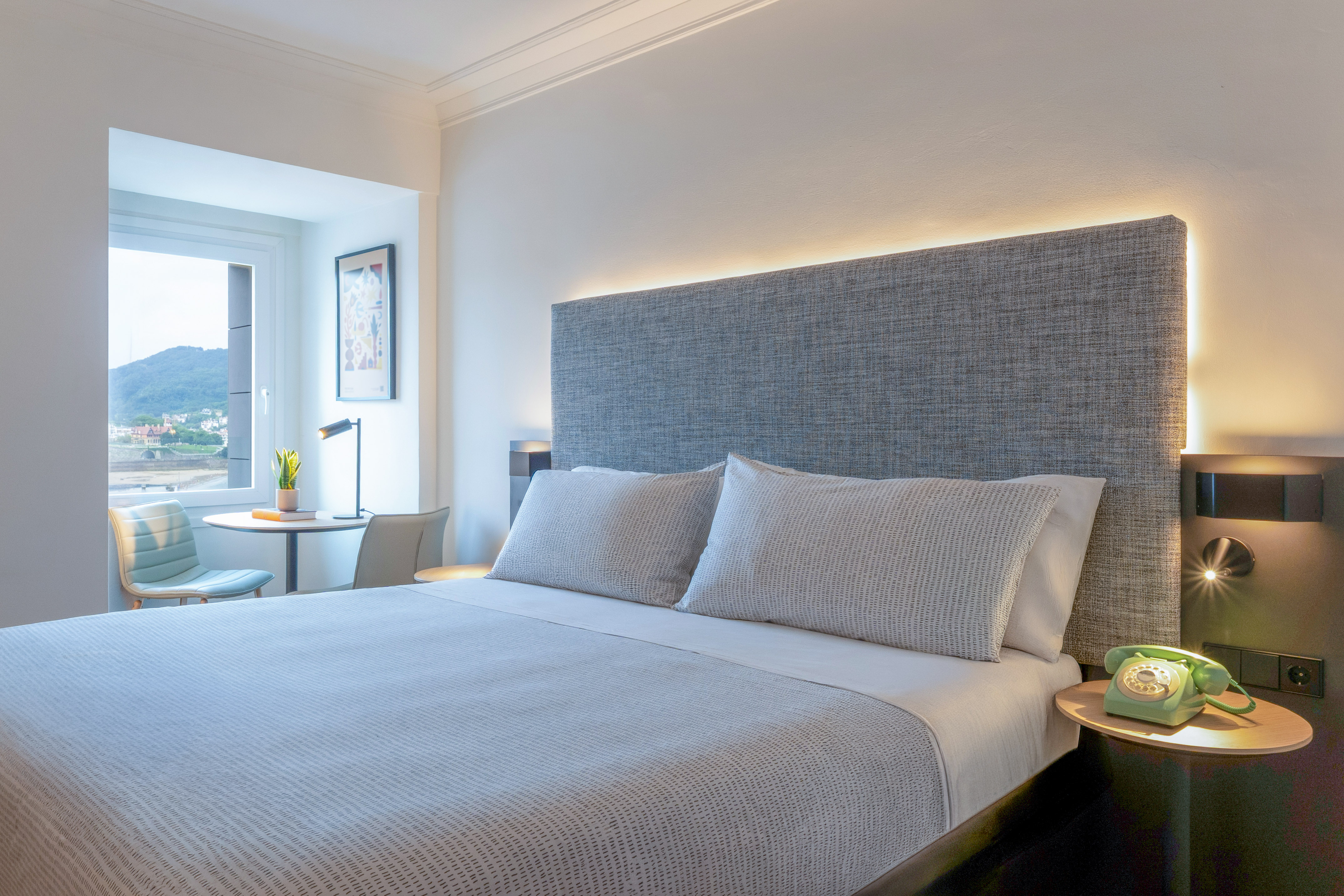 Habitación de hotel moderna con cama doble, cabecero iluminado y vista al mar.