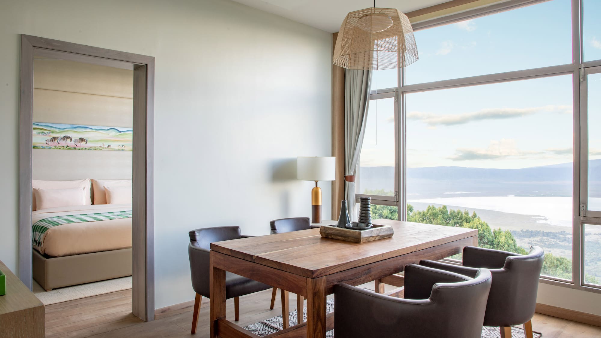 Modern dining area with lake view through large windows, adjoining bedroom.