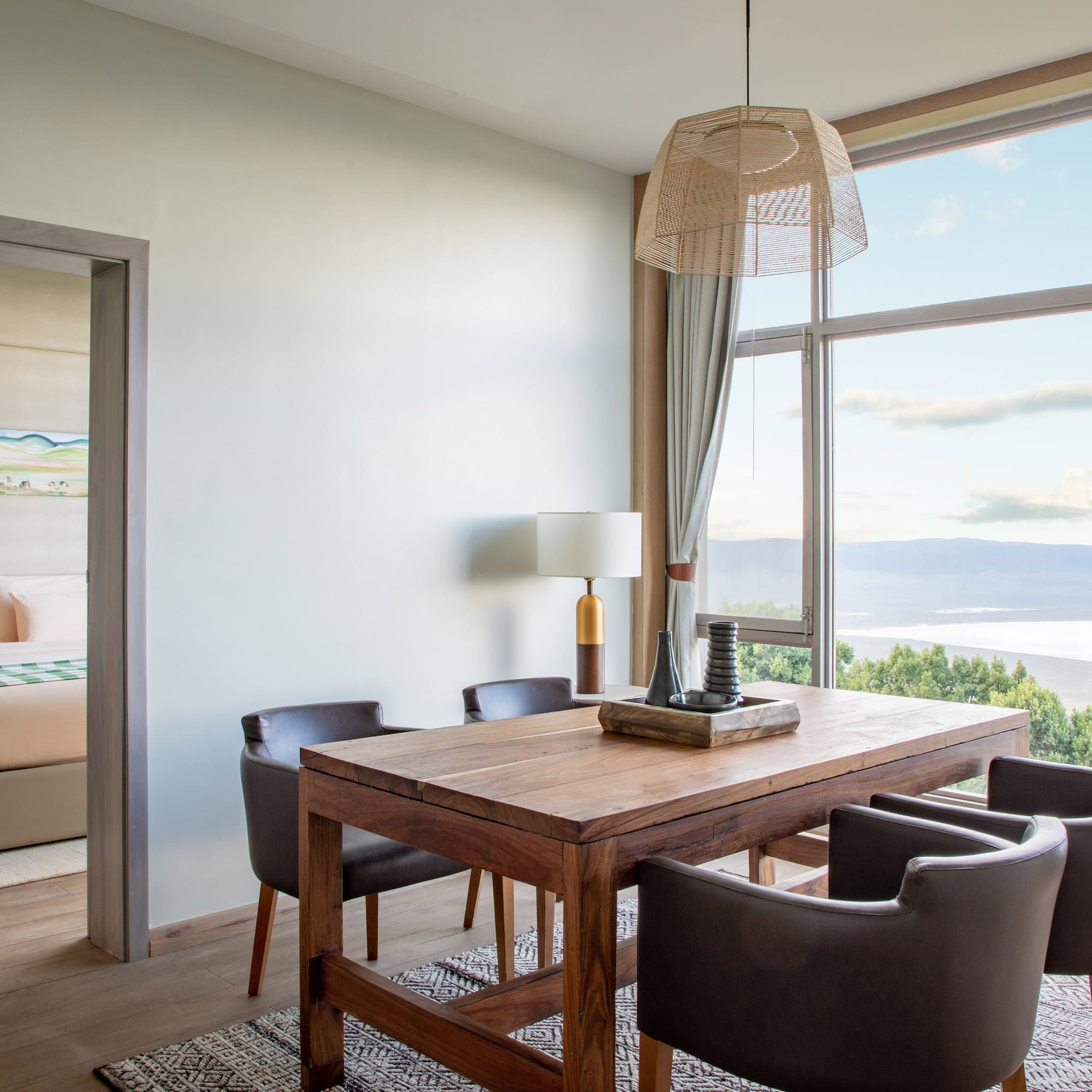 Modern dining area with lake view through large windows, adjoining bedroom.