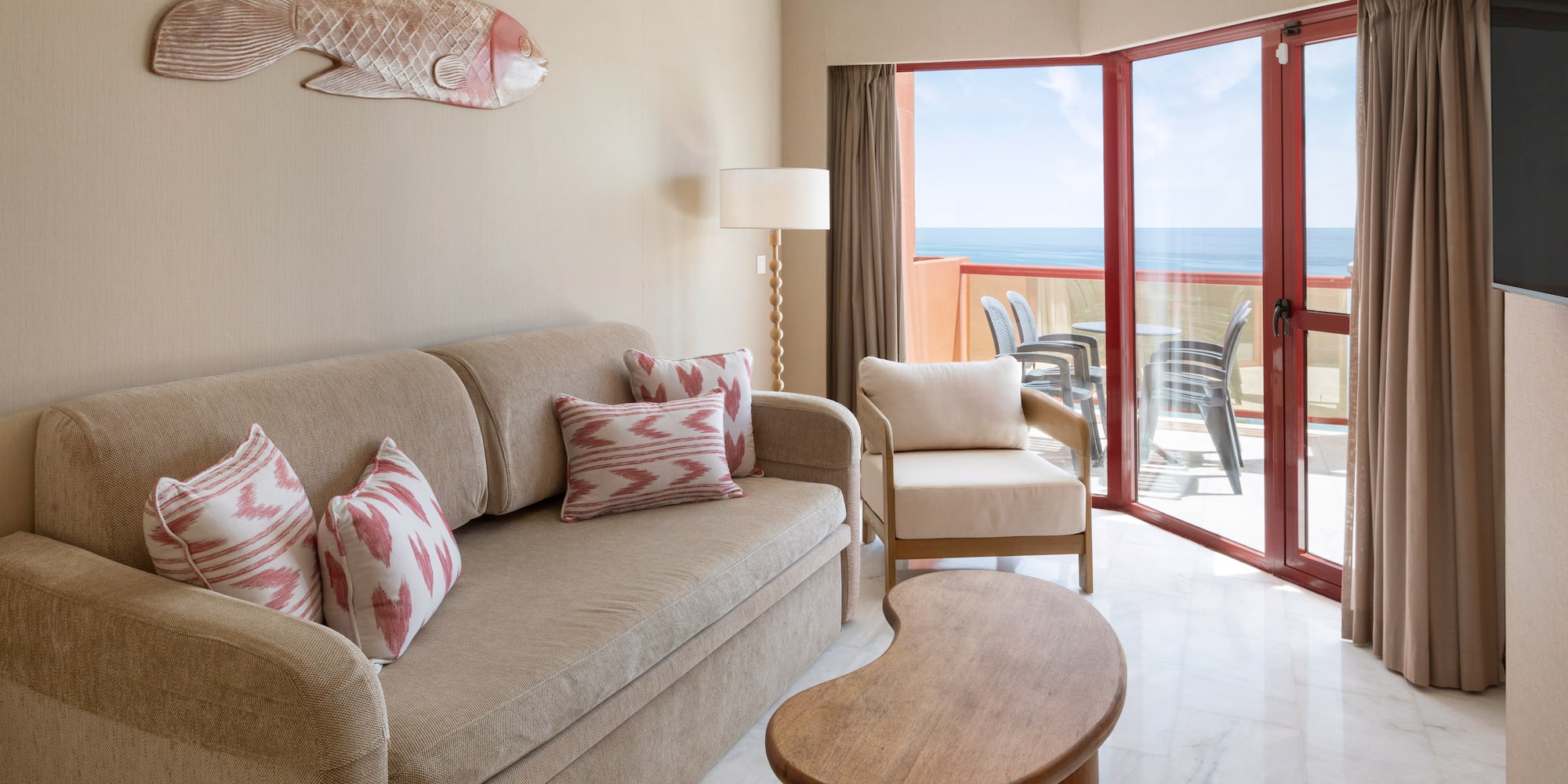 Hotel suite living room with ocean view, beige sofa, and balcony access.
