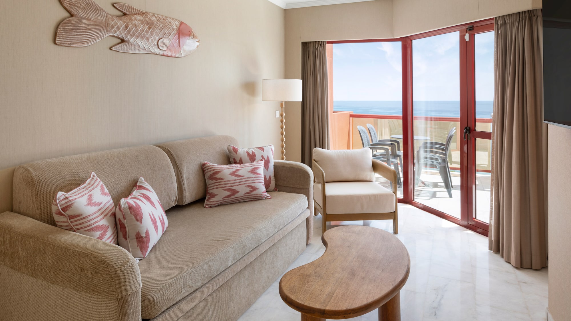 Ocean view hotel suite living room with sofa, balcony, and coastal fish art.