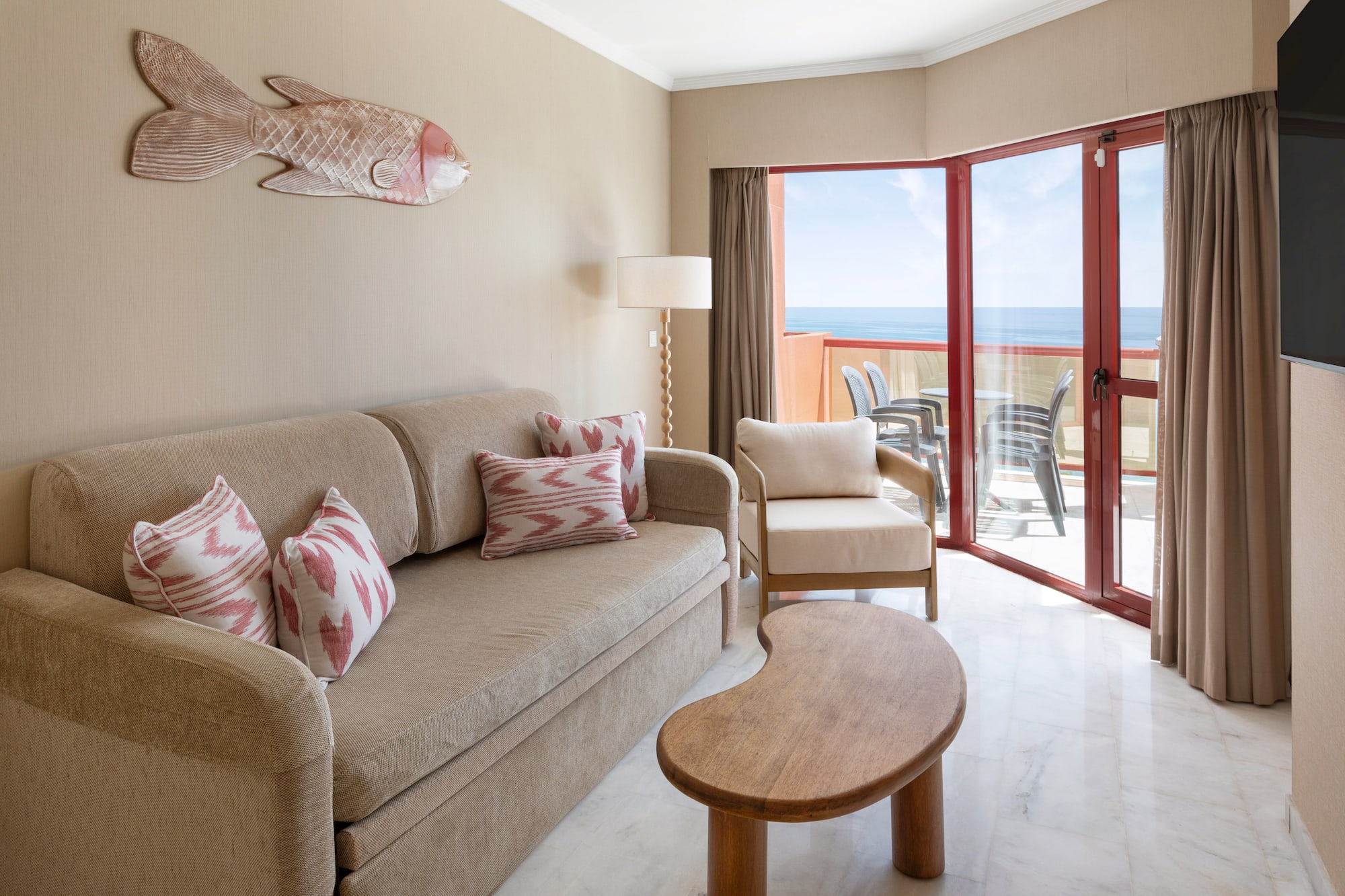 Hotel suite living room with ocean view, beige sofa, and balcony access.