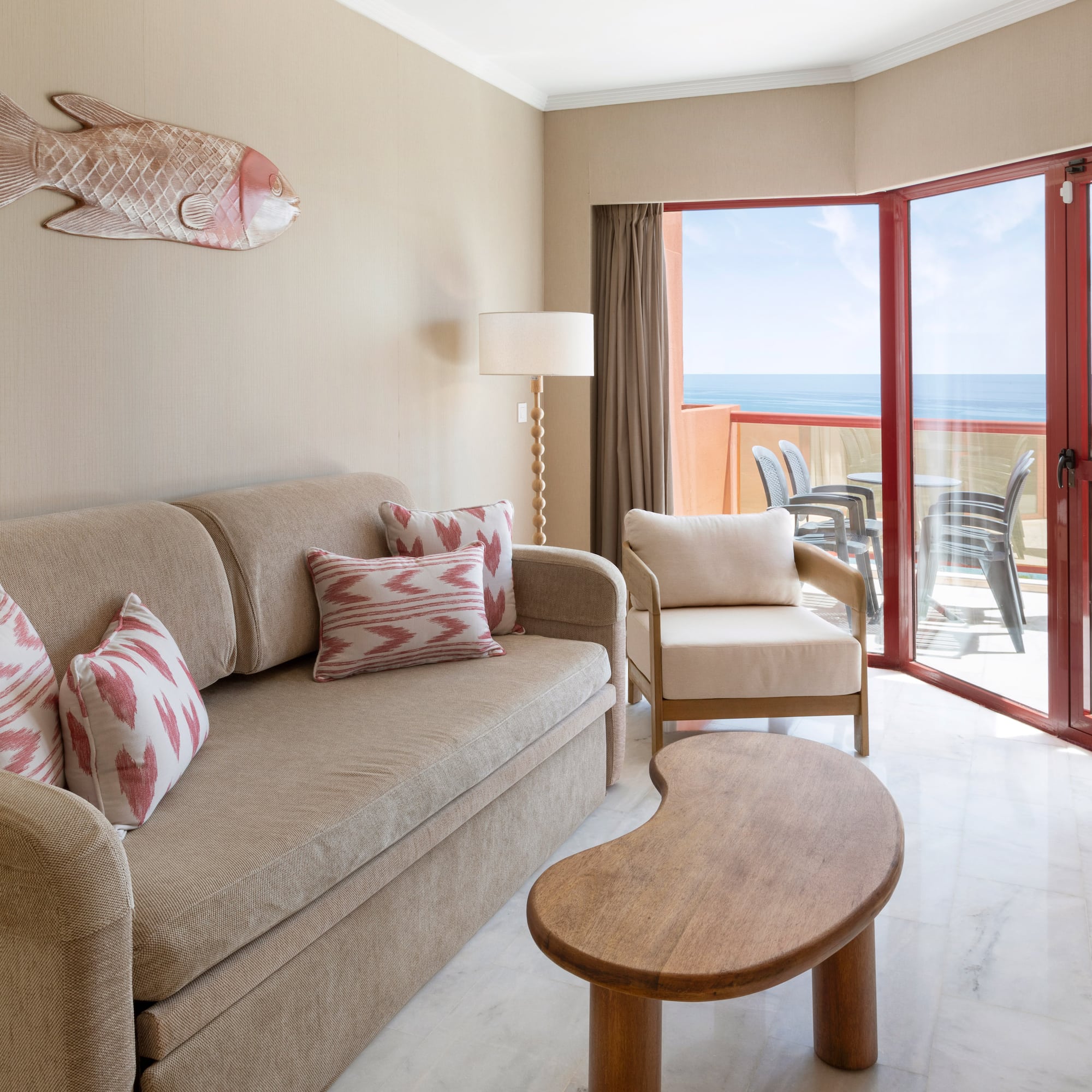 Ocean view hotel suite living room with sofa, balcony, and coastal fish art.