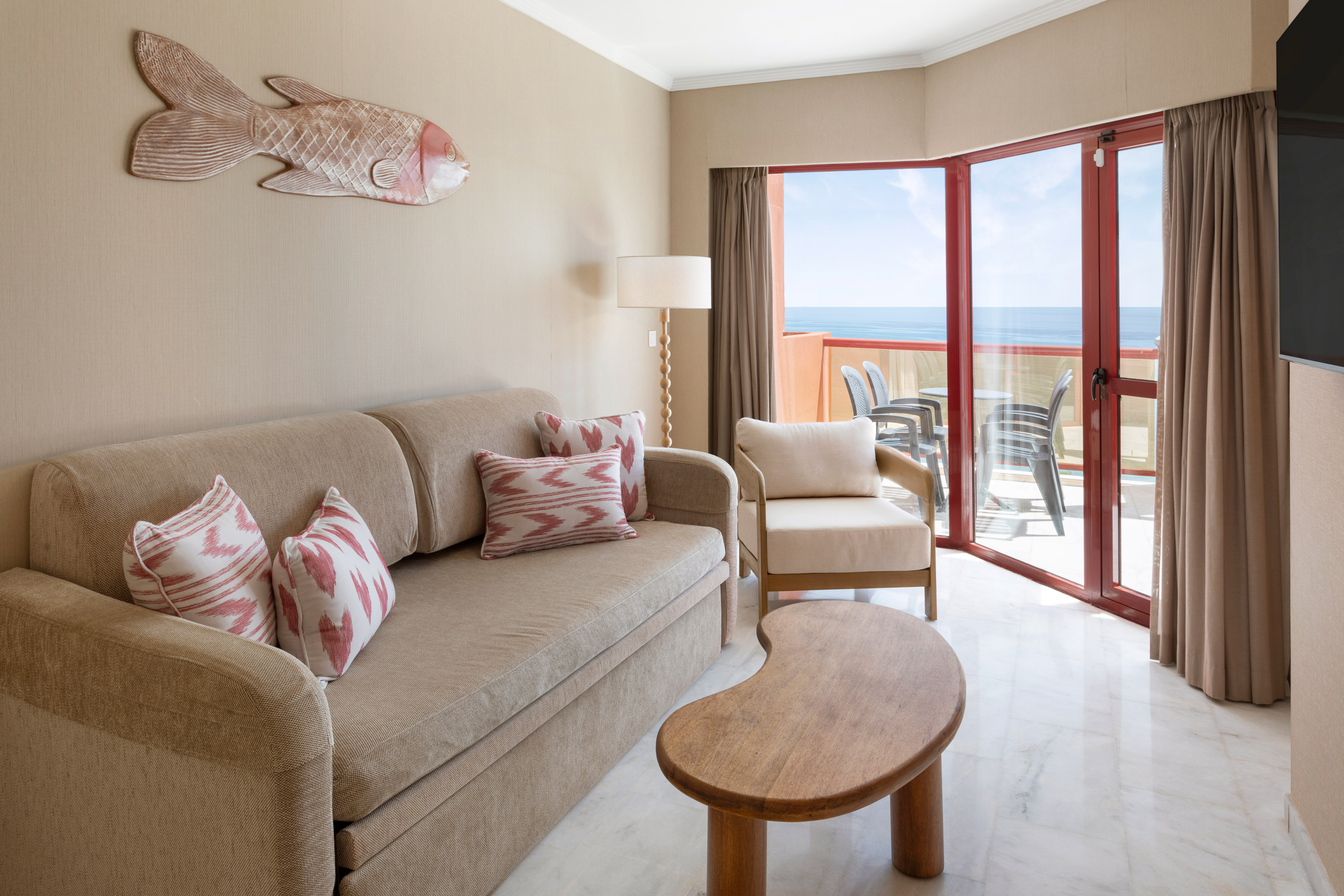 Ocean view hotel suite living room with sofa, balcony, and coastal fish art.