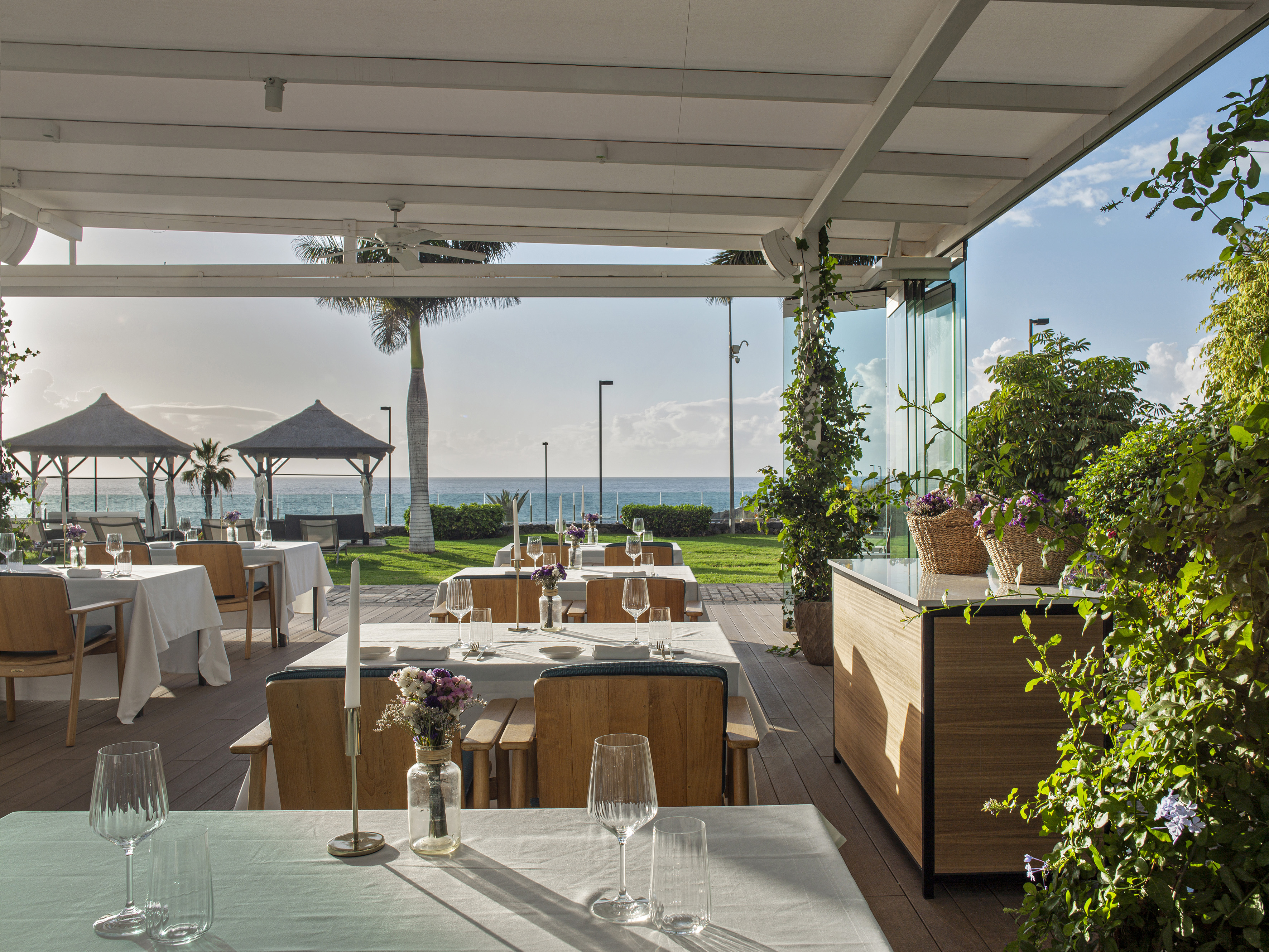 Beachfront outdoor restaurant patio with dining tables and ocean view.