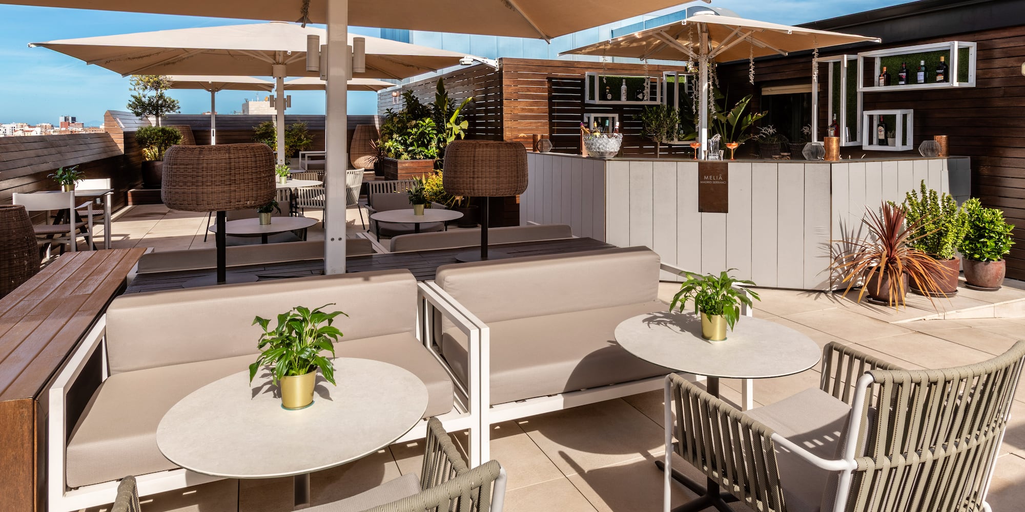 Sunny rooftop bar with beige umbrellas, lounge seating, and a modern bar counter.
