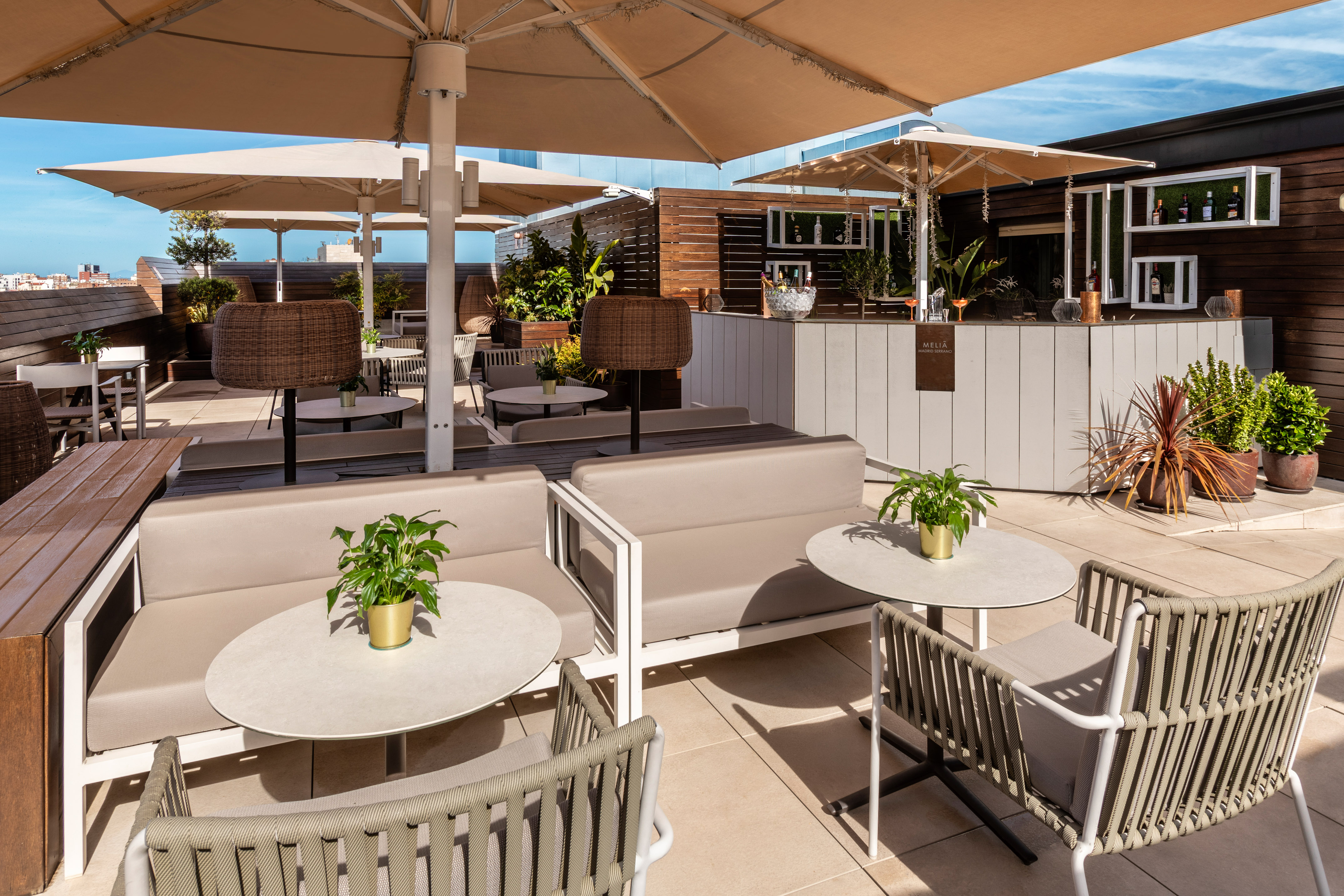 Sunny rooftop bar with beige umbrellas, lounge seating, and a modern bar counter.