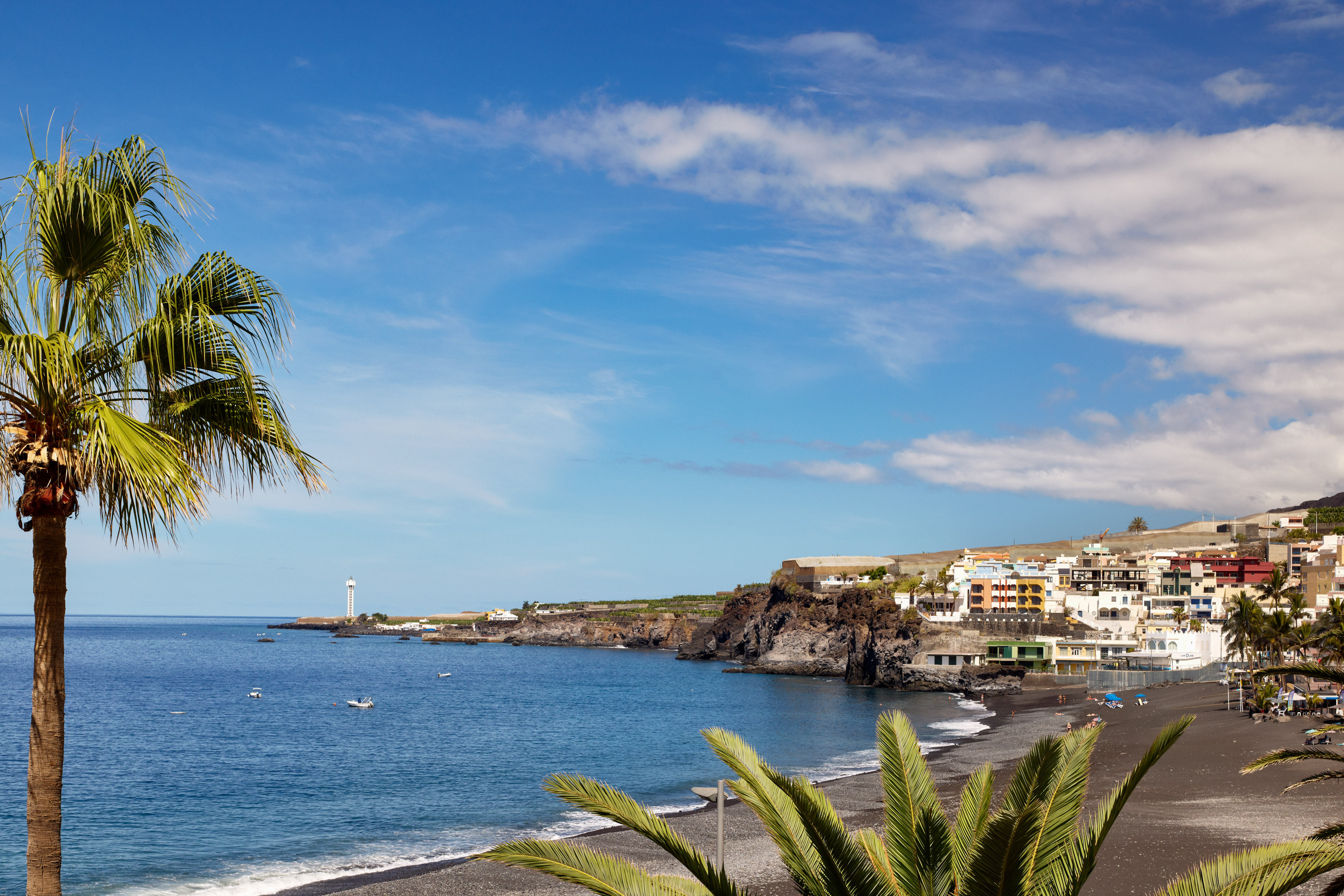 Black sand beach, colorful coastal village, ocean, palm trees, lighthouse.
