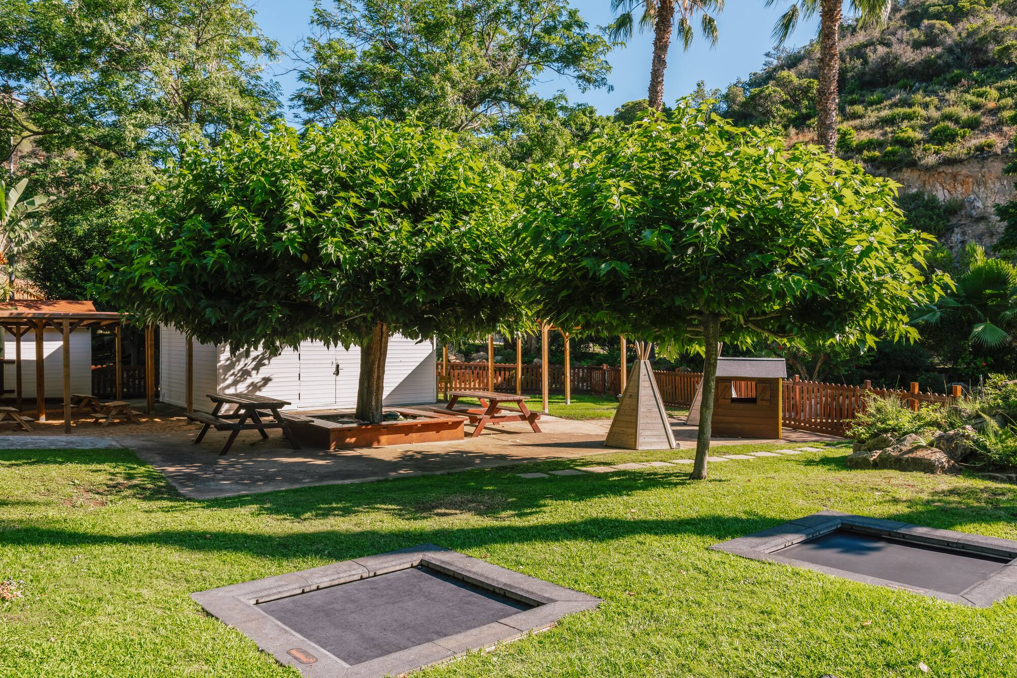 Grassy outdoor play area with in-ground trampolines, picnic tables, and shade trees.