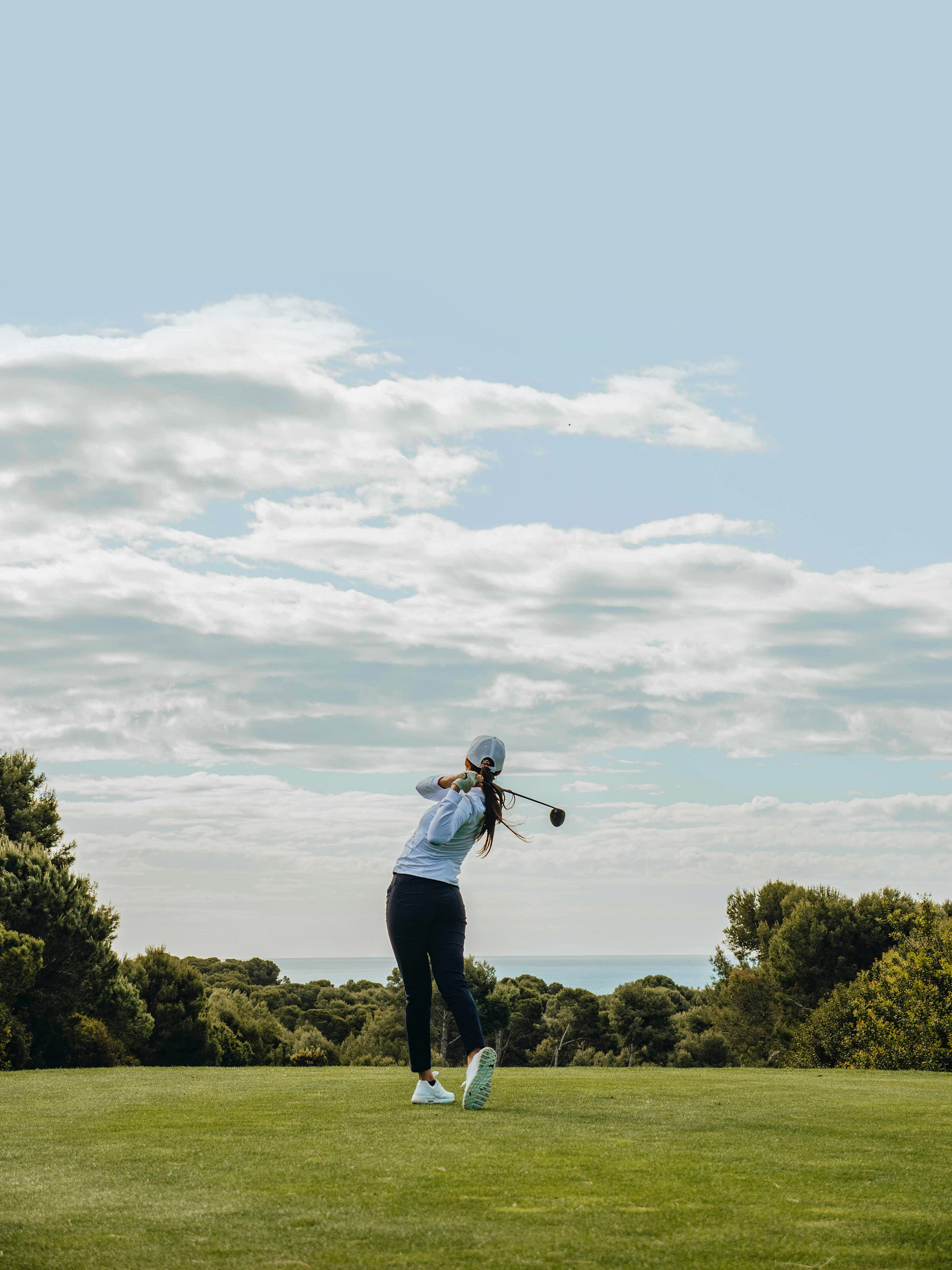 Female golfer driving on a scenic golf course by the sea.