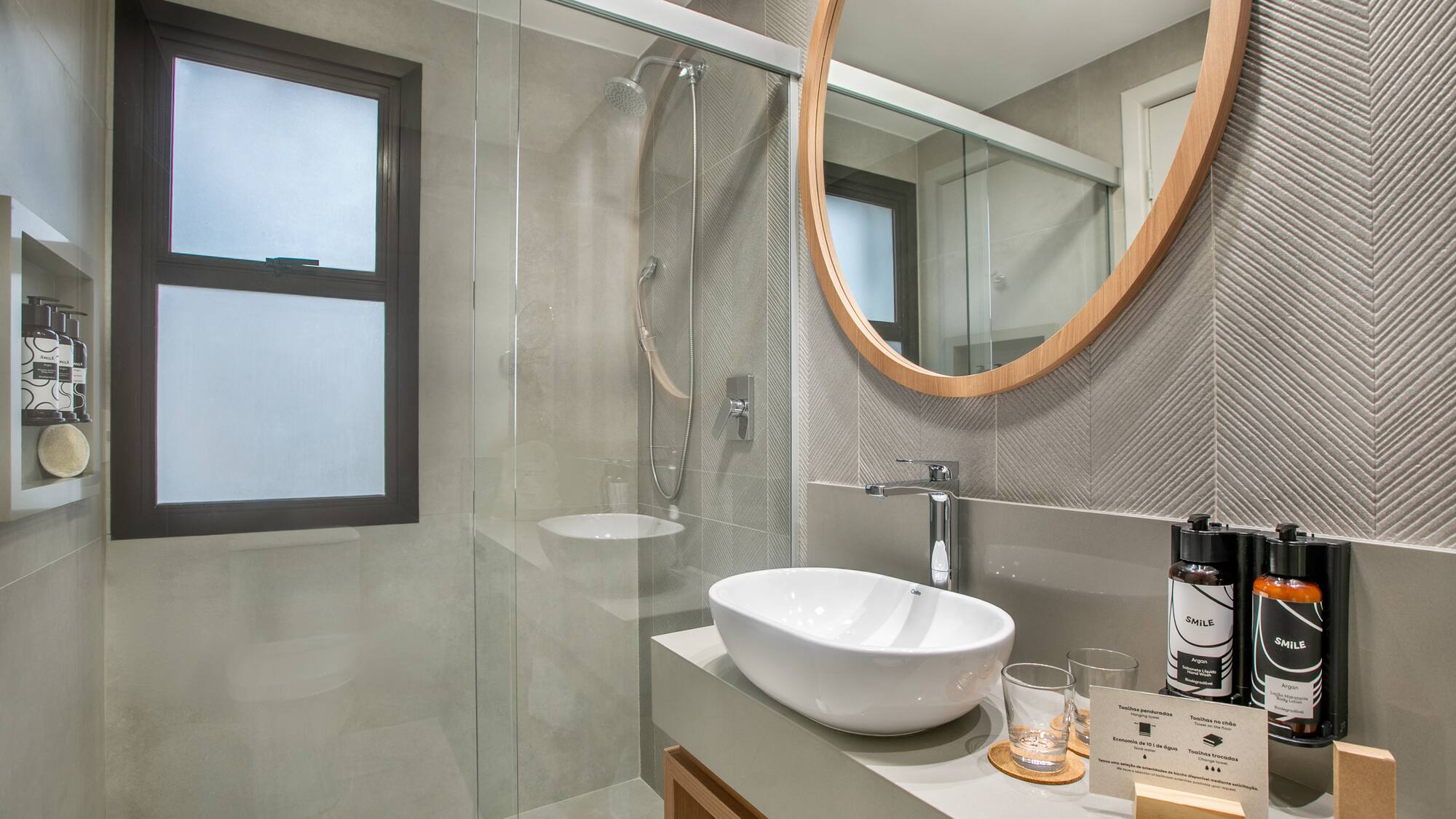 Stylish grey bathroom with walk-in shower, round mirror, and vessel sink.