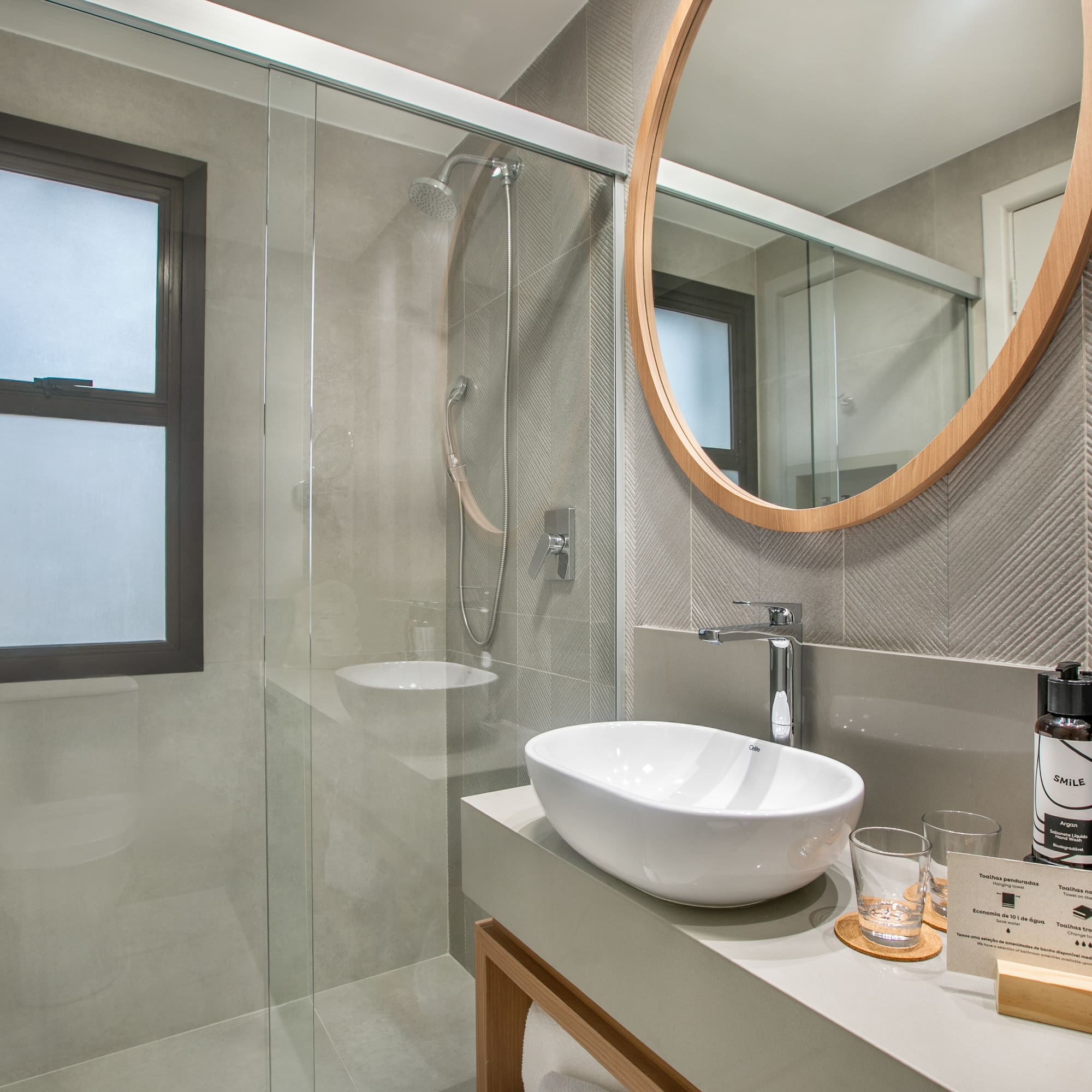 Baño moderno con lavabo sobre encimera, espejo redondo y ducha de cristal.