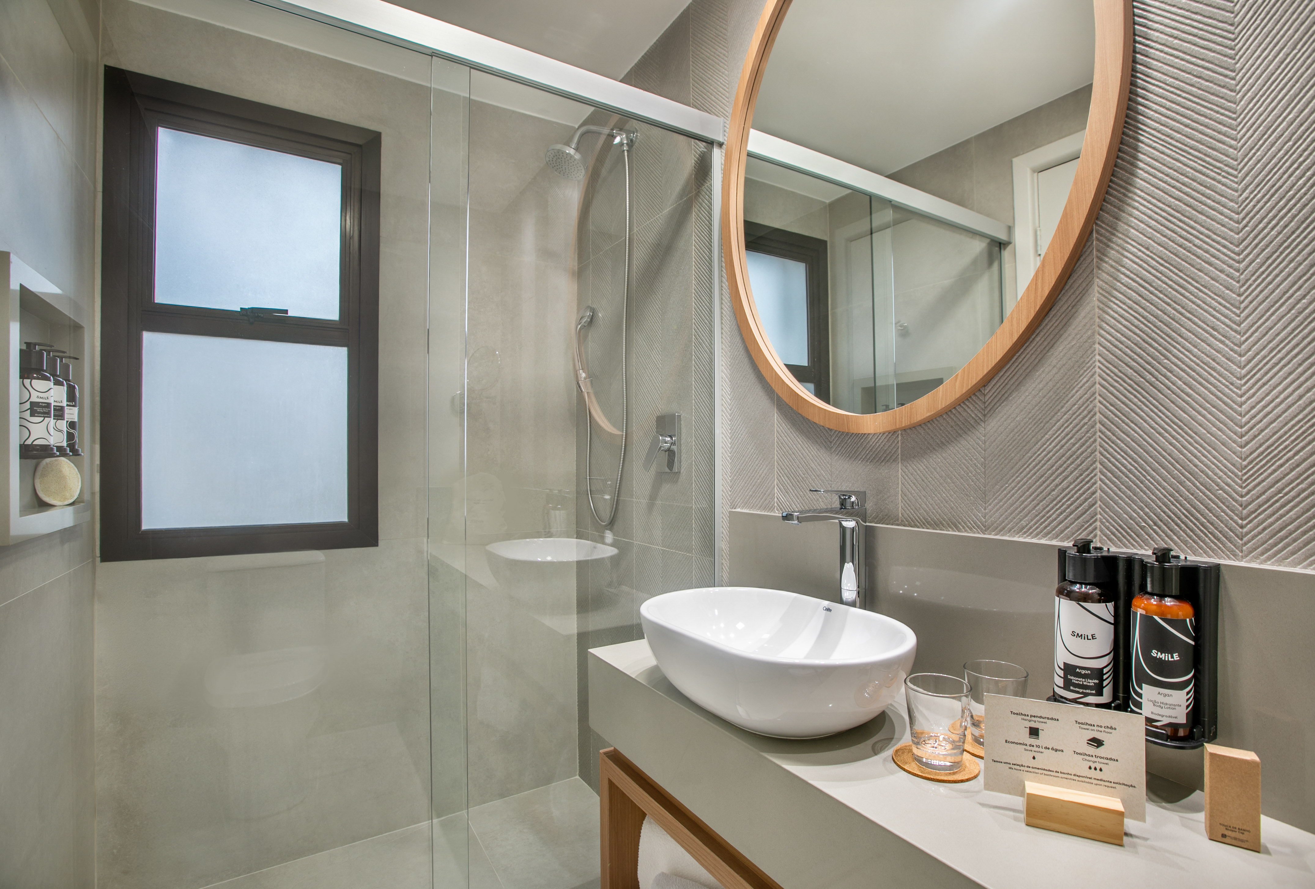 Baño moderno con lavabo sobre encimera, espejo redondo y ducha de cristal.