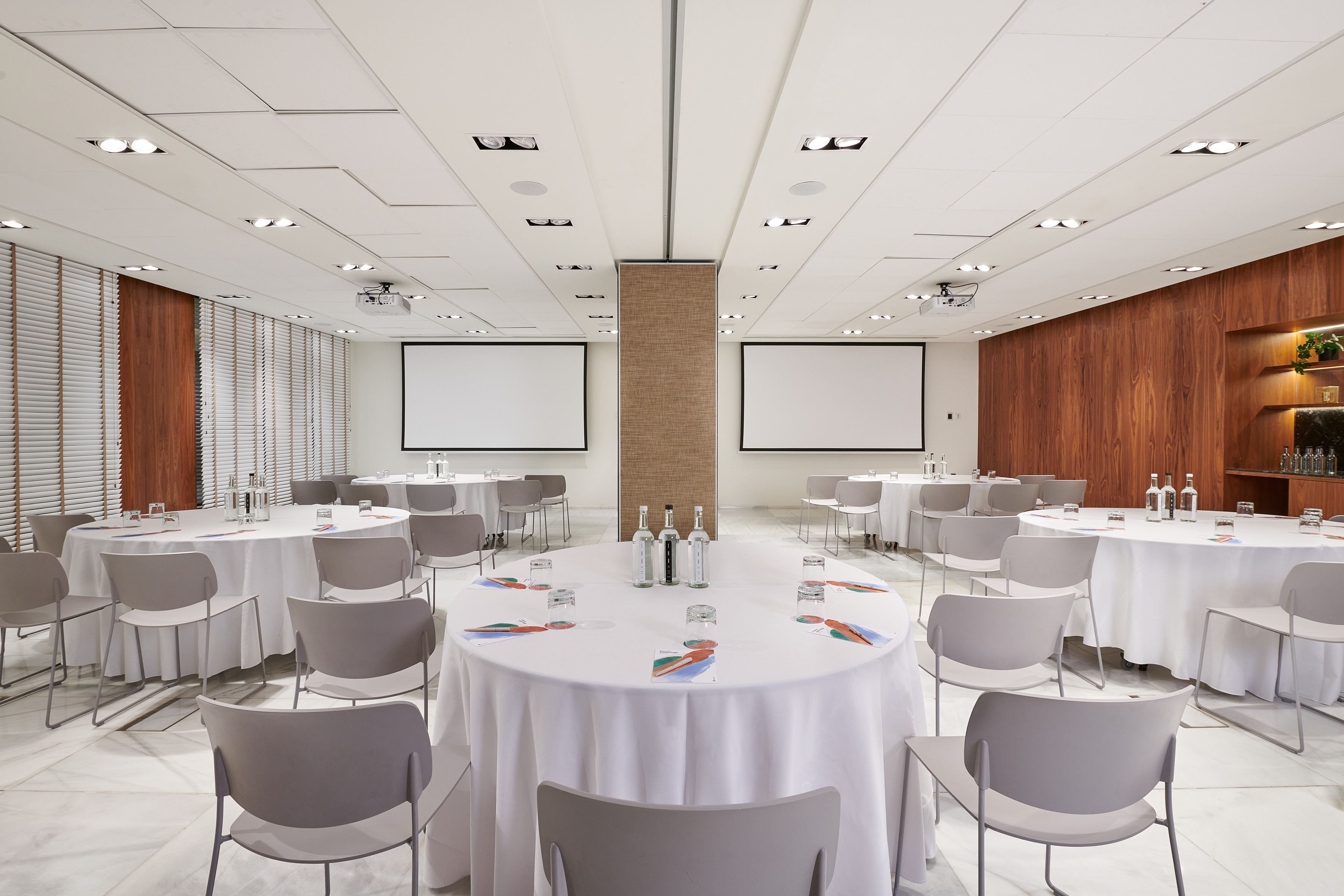 Modern meeting space with round tables, chairs, and dual projection screens.