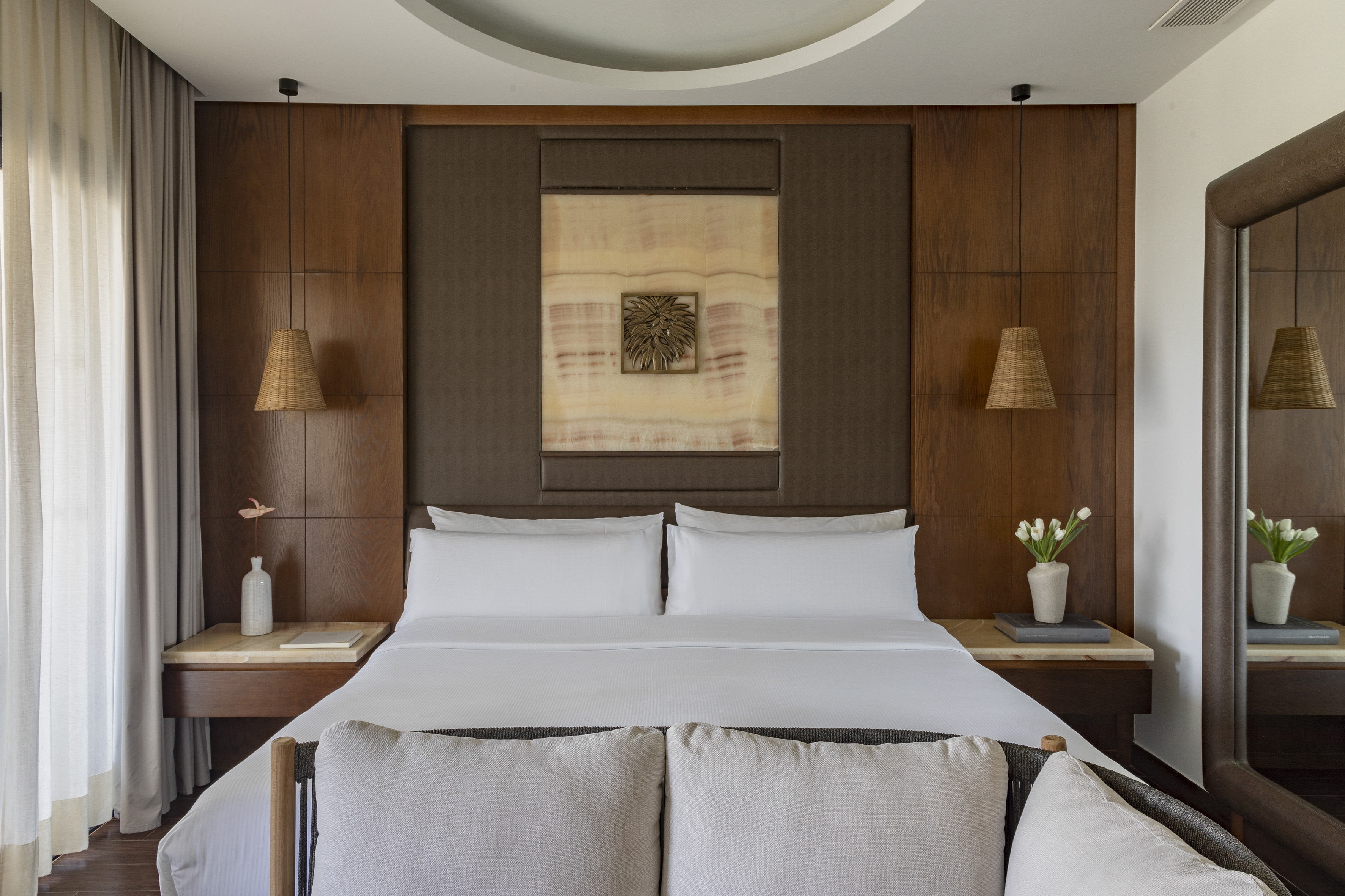 Luxury hotel bedroom with king bed, wood paneling, onyx art, and wicker lamps.