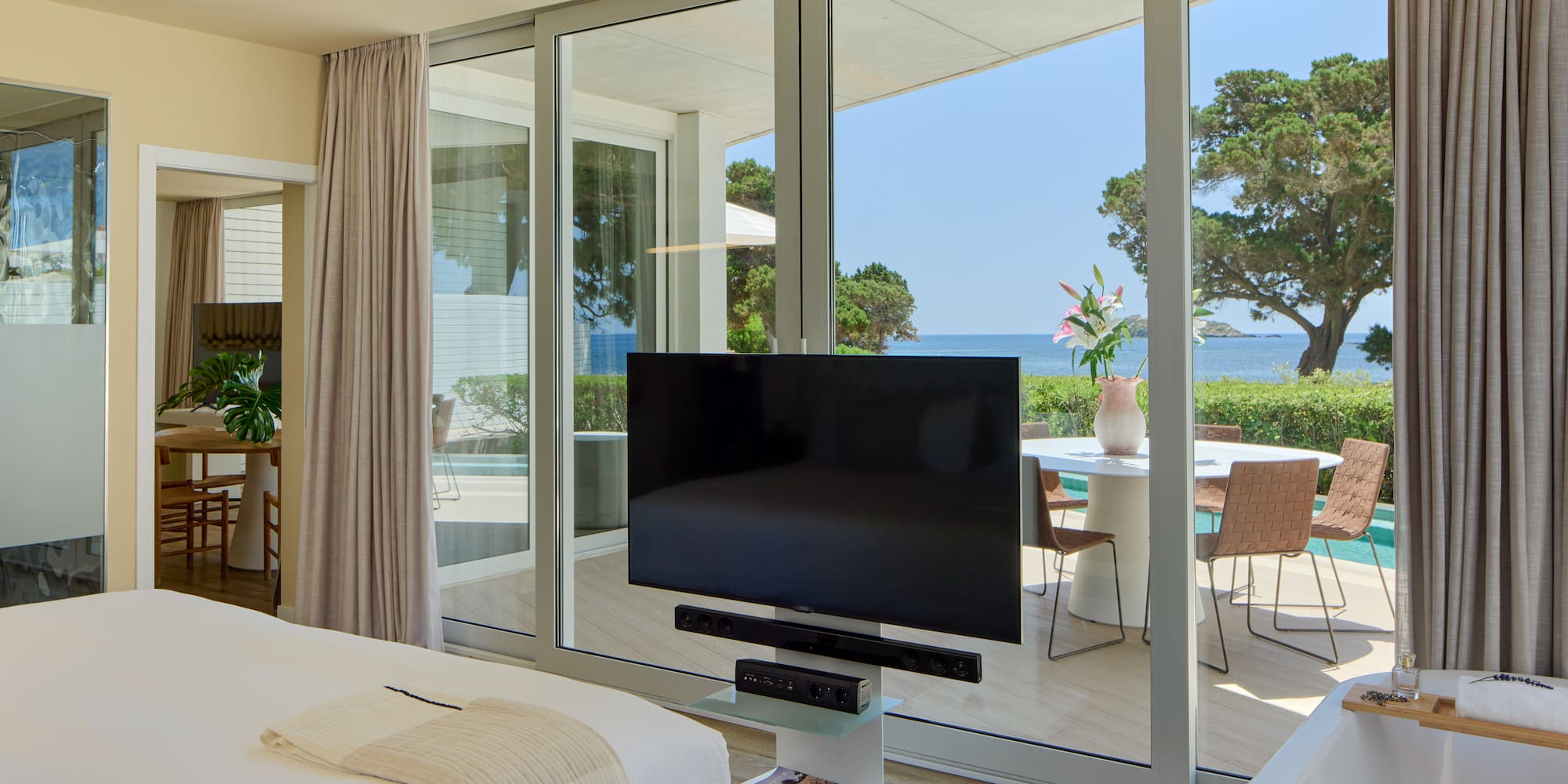 Modern hotel bedroom with ocean view, large TV, and private terrace.