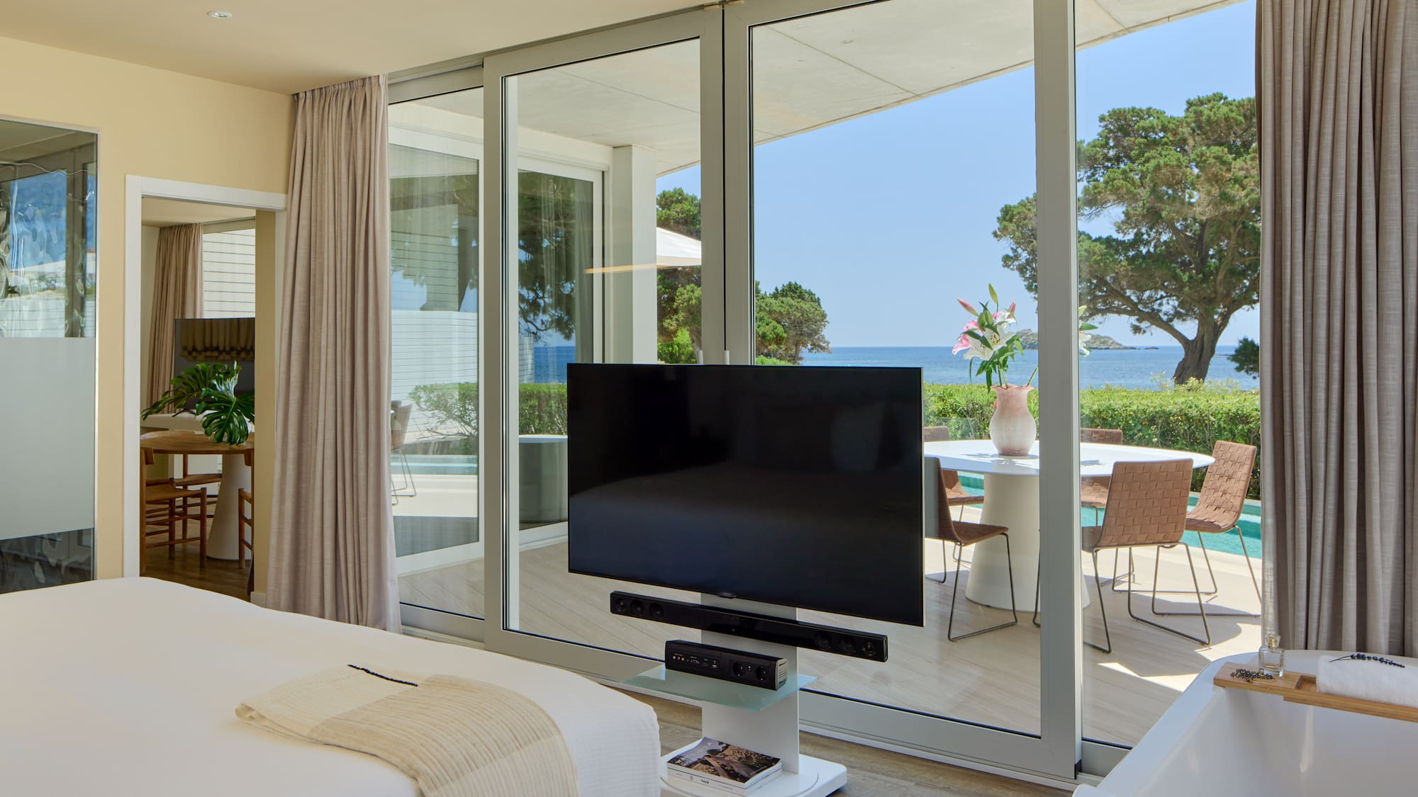 Modern hotel bedroom with ocean view, large TV, and private terrace.
