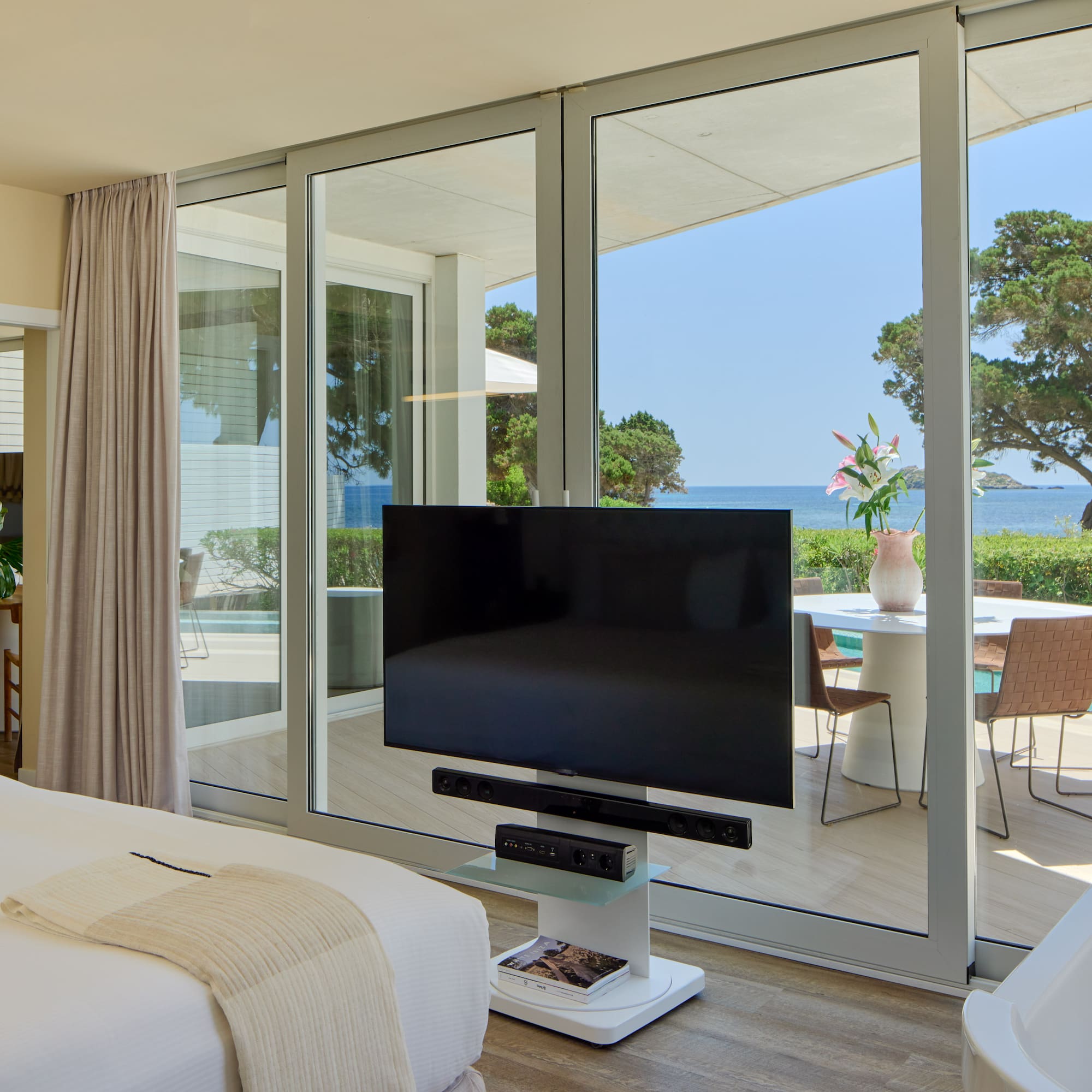Modern hotel bedroom with ocean view, large TV, and private terrace.