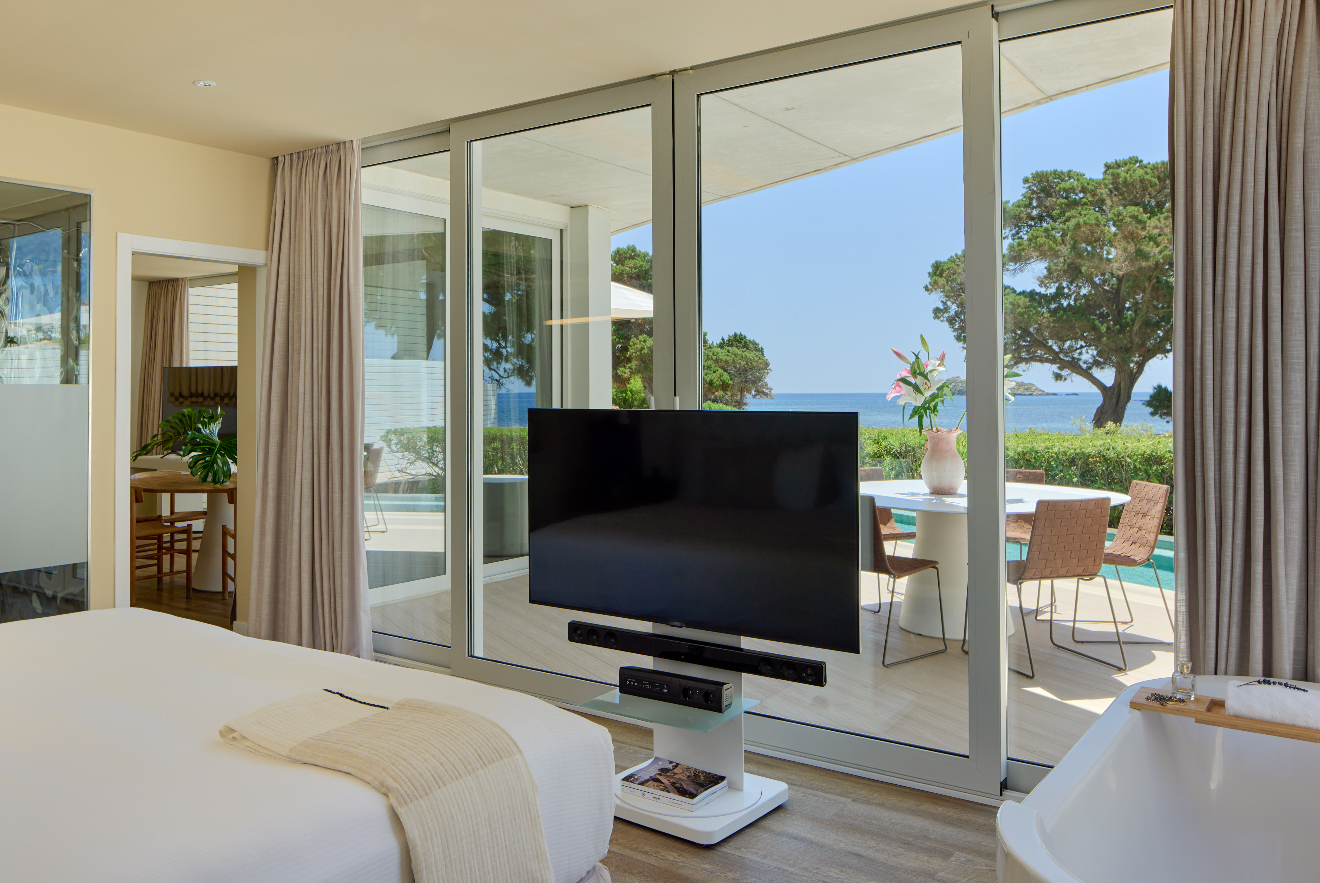Modern hotel bedroom with ocean view, large TV, and private terrace.