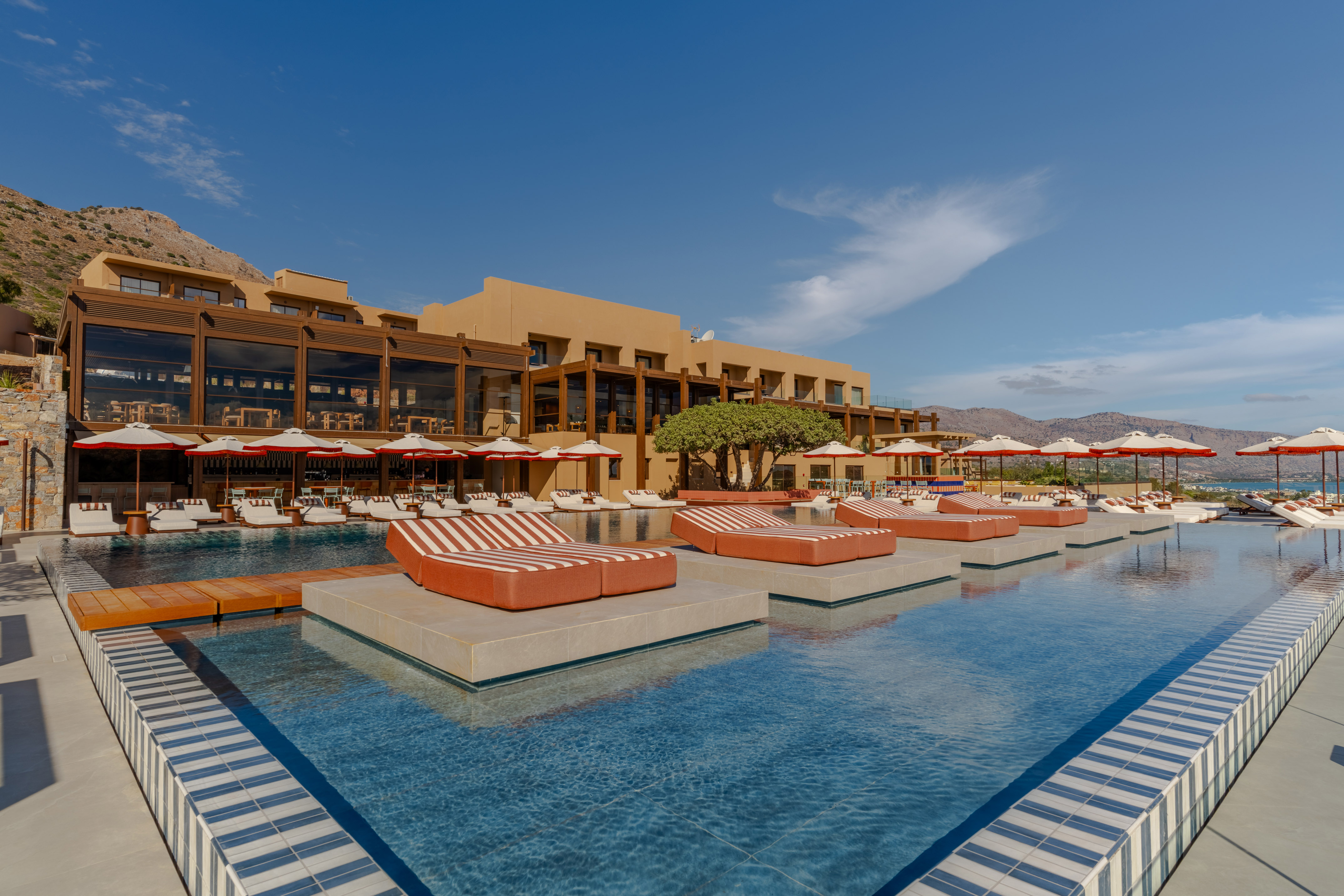 Modern luxury resort with swimming pool, striped lounge beds, and mountain views.