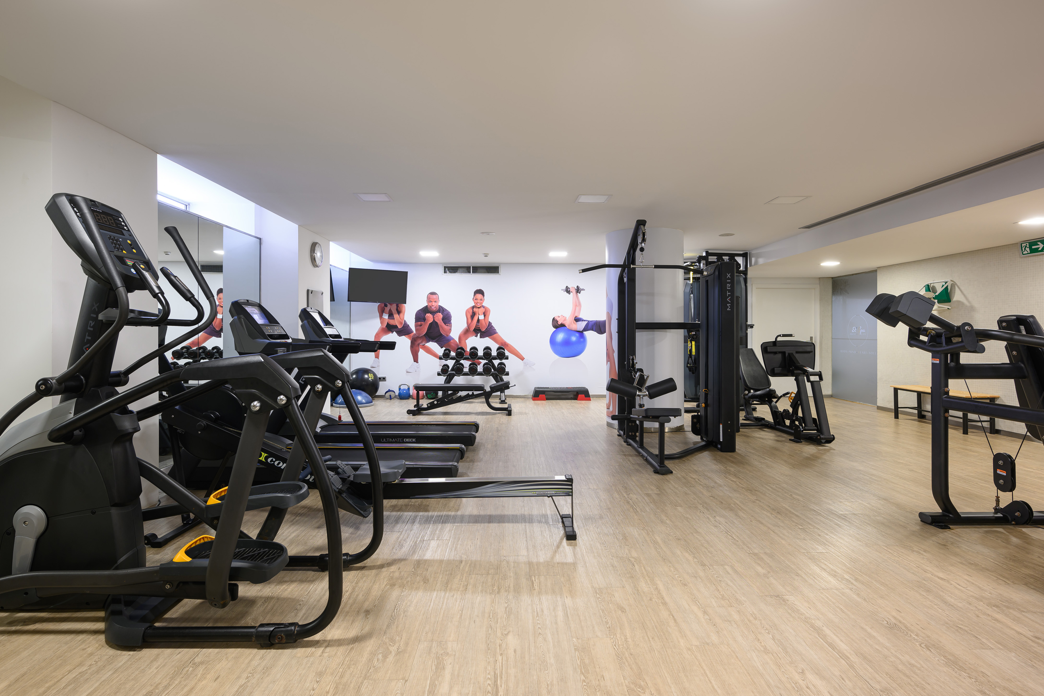 Bright modern gym with ellipticals, treadmills, weights, and motivational wall murals.