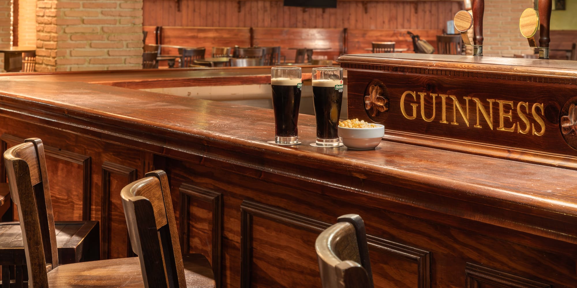 Two Guinness stout beers and snacks on a polished wooden pub bar.