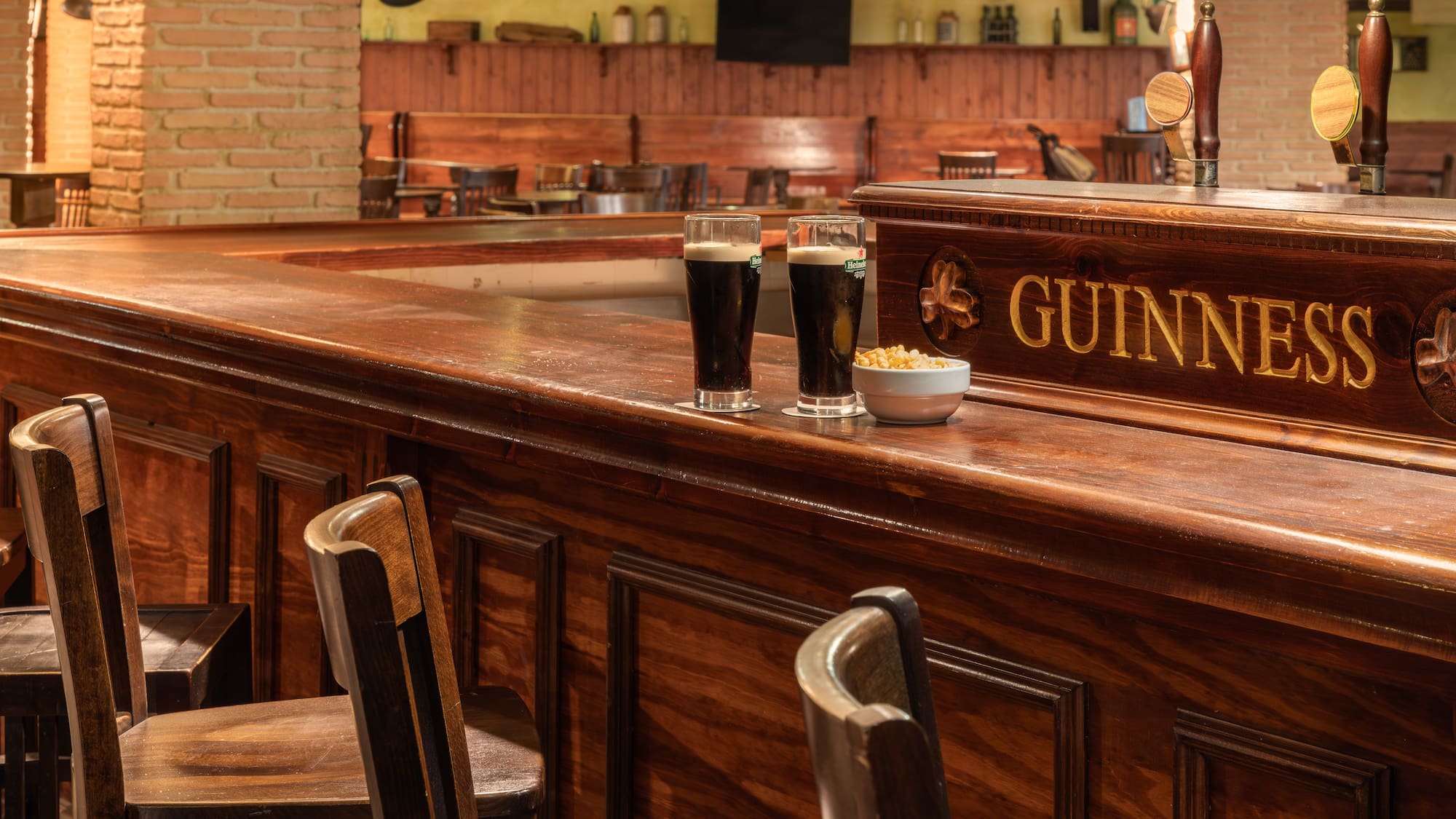 Two Guinness stout beers and snacks on a polished wooden pub bar.